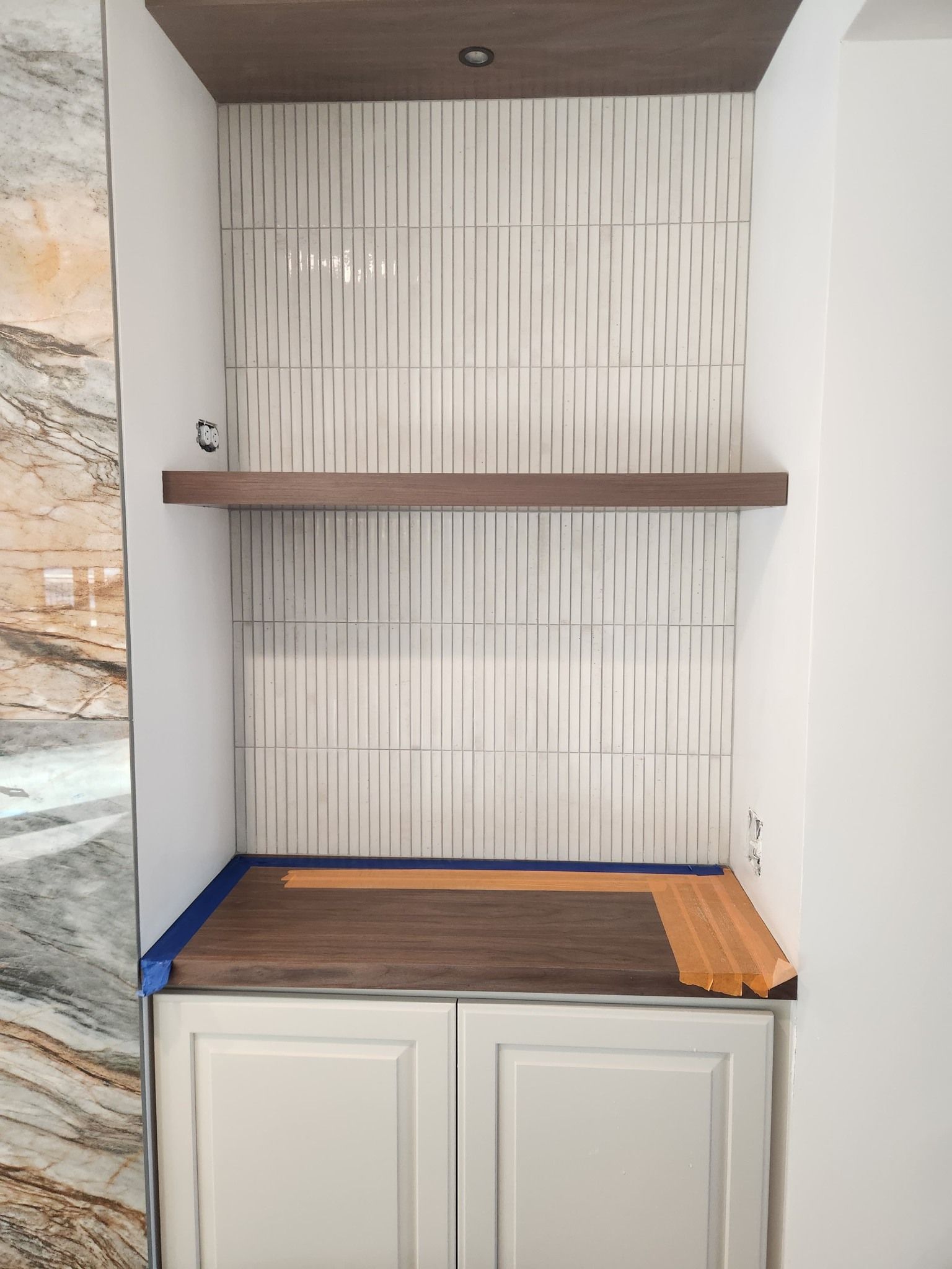 White subway tile fireplace backsplash with brown wood mantel shelf and wood-look bench underneath.