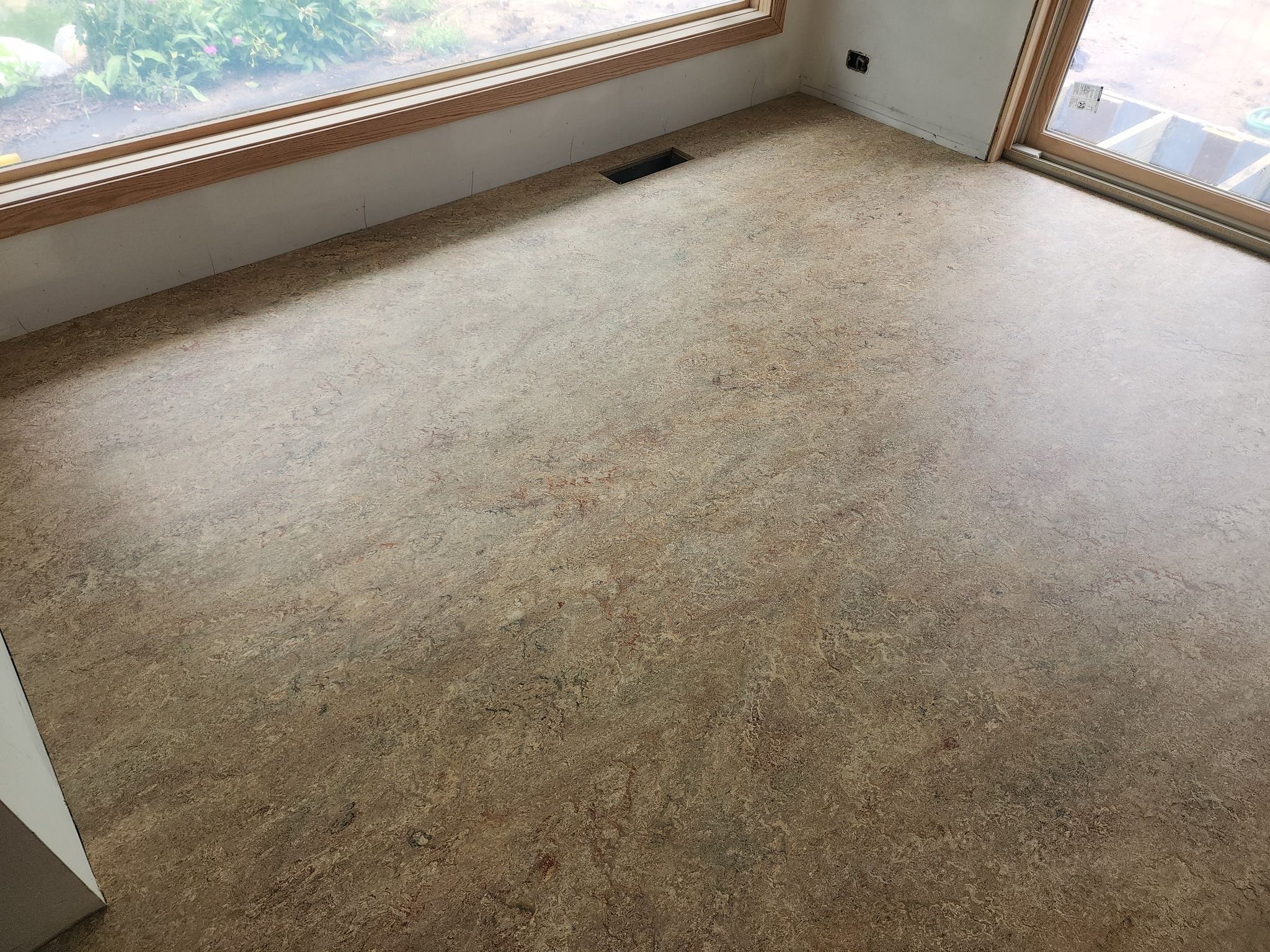 Empty bedroom with tan and brown LVP flooring and large windows overlooking outdoor scenery.