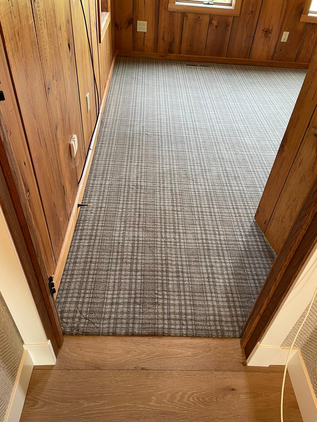 Gray wool carpet with grid weave pattern installed in hallway between wood-paneled walls.