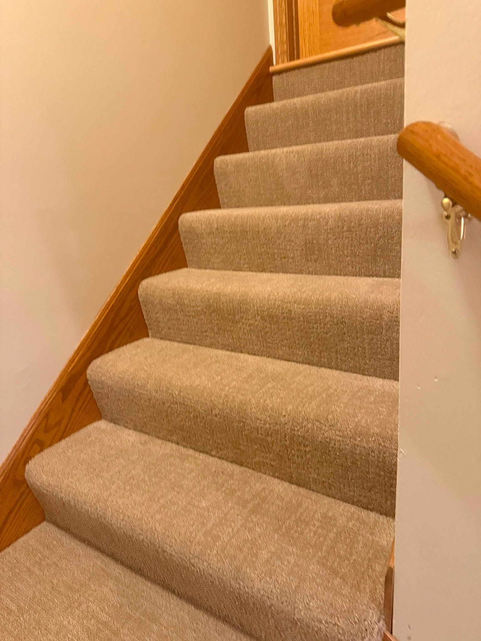 Beige carpet installed on staircase with wood railings and stringer.