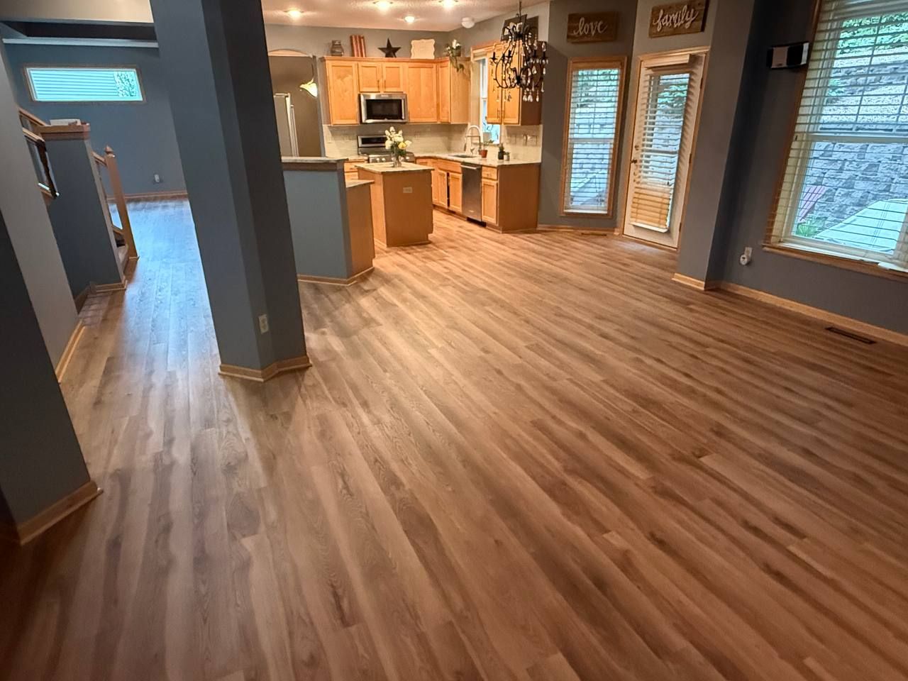 Stained hickory hardwood flooring in kitchen and living area with wood cabinetry and large windows.