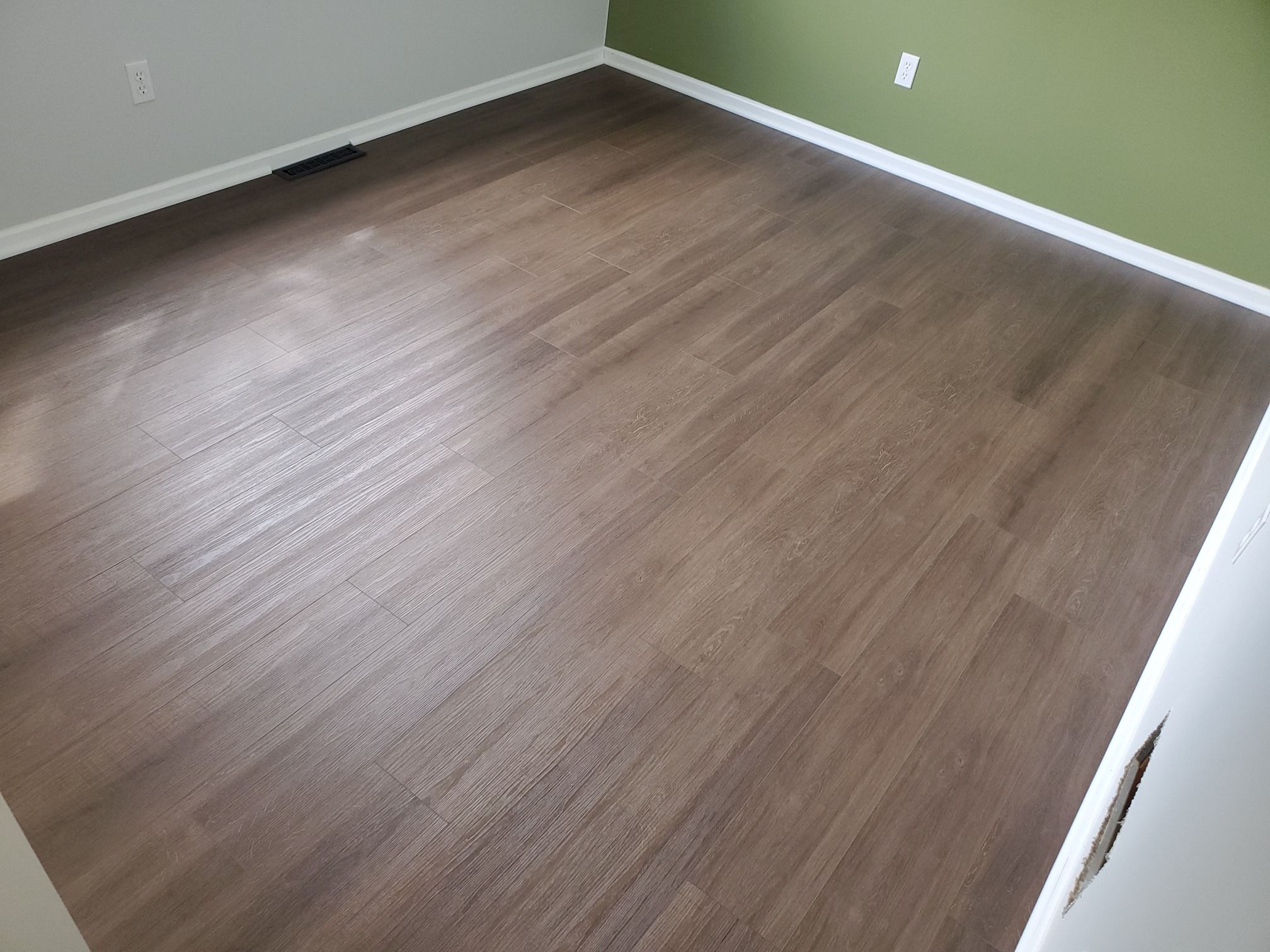 Luxury vinyl plank flooring in medium brown installed in a bedroom with white trim and green painted walls.