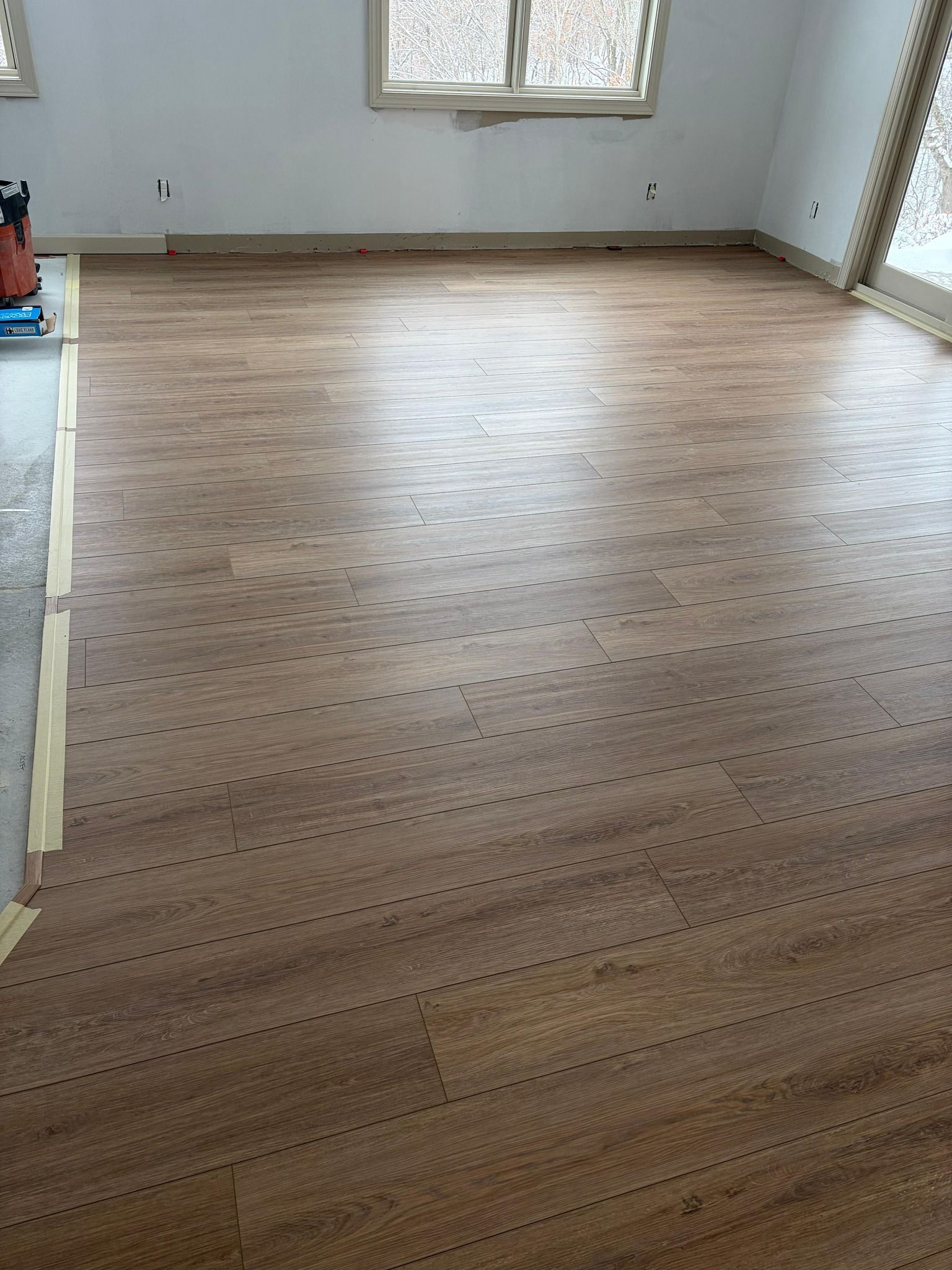 Newly installed medium-toned wood-look luxury vinyl plank flooring in an empty room with large windows.
