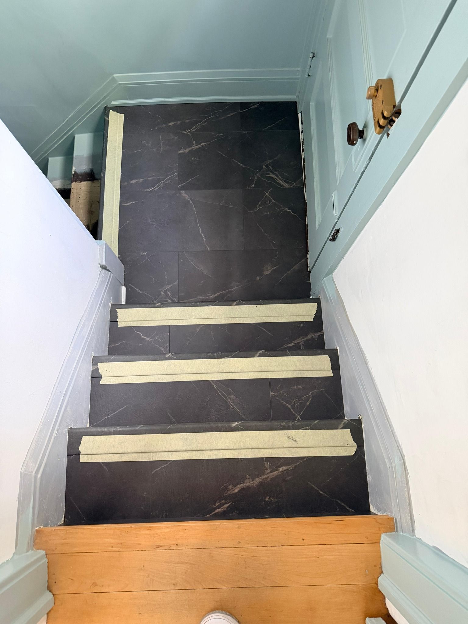 LVP stairs with black marble-look planks and tan stair nosings installed over wooden treads in basement stairwell.
