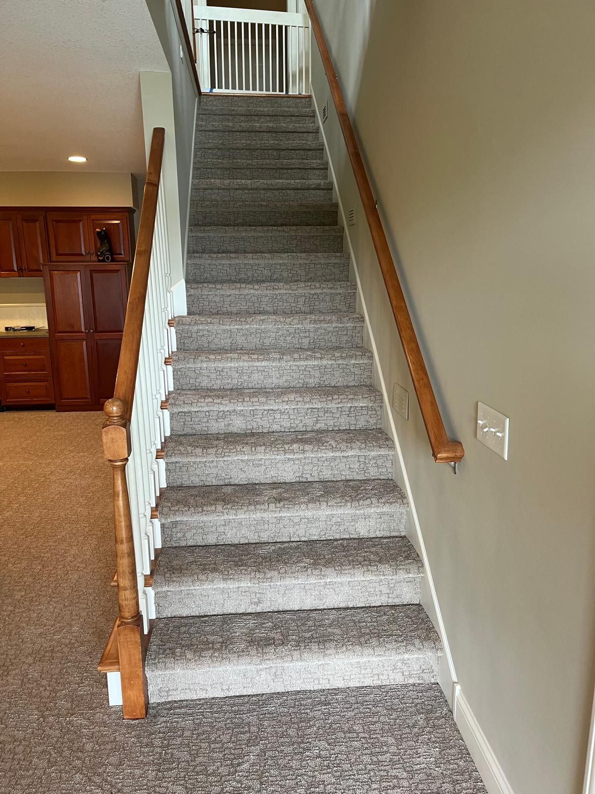 Gray carpet installed on basement stairs with wood handrail and white balusters.