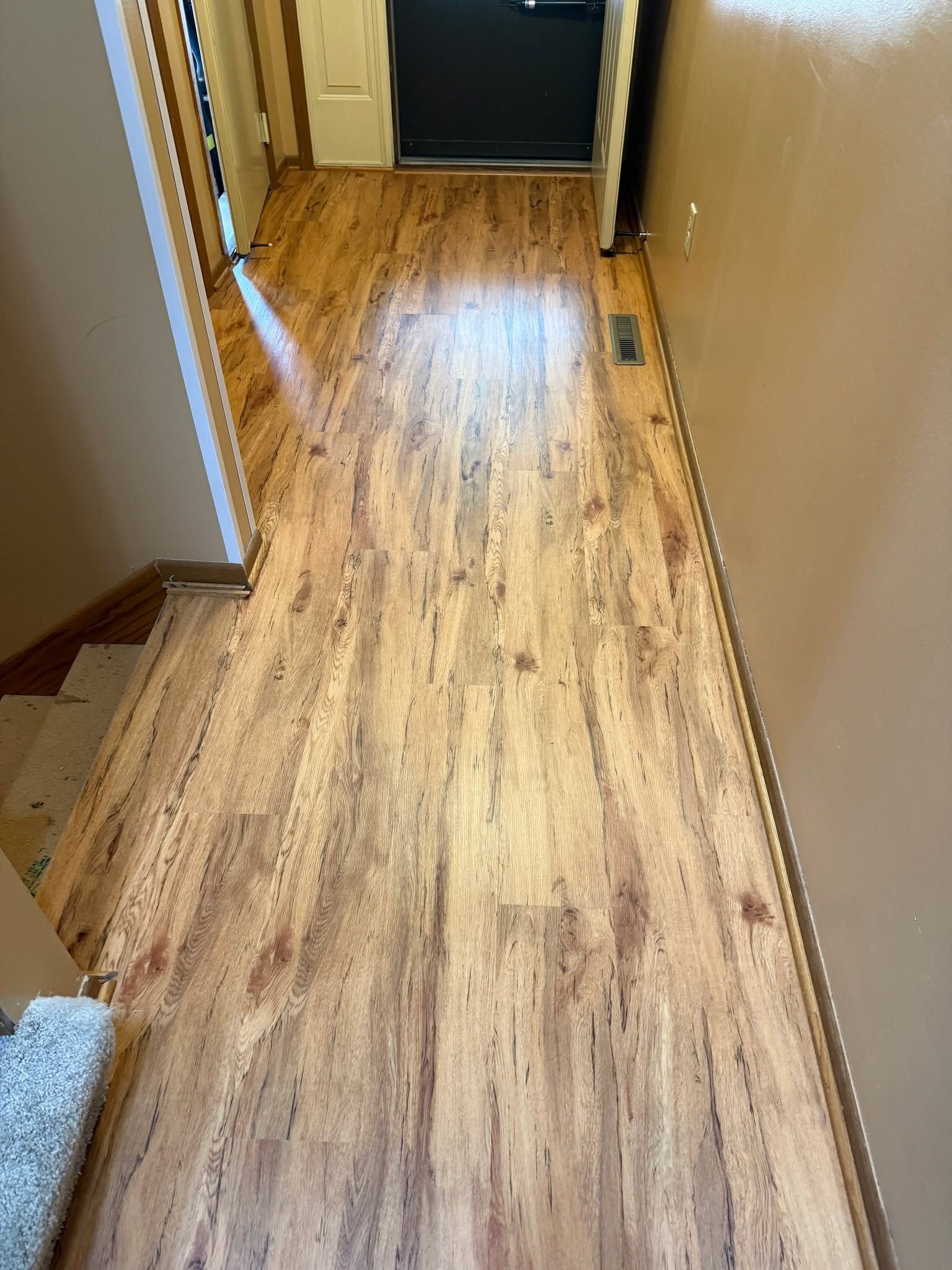 Hallway with medium-tone wood-look luxury vinyl plank flooring installed between white and beige walls.
