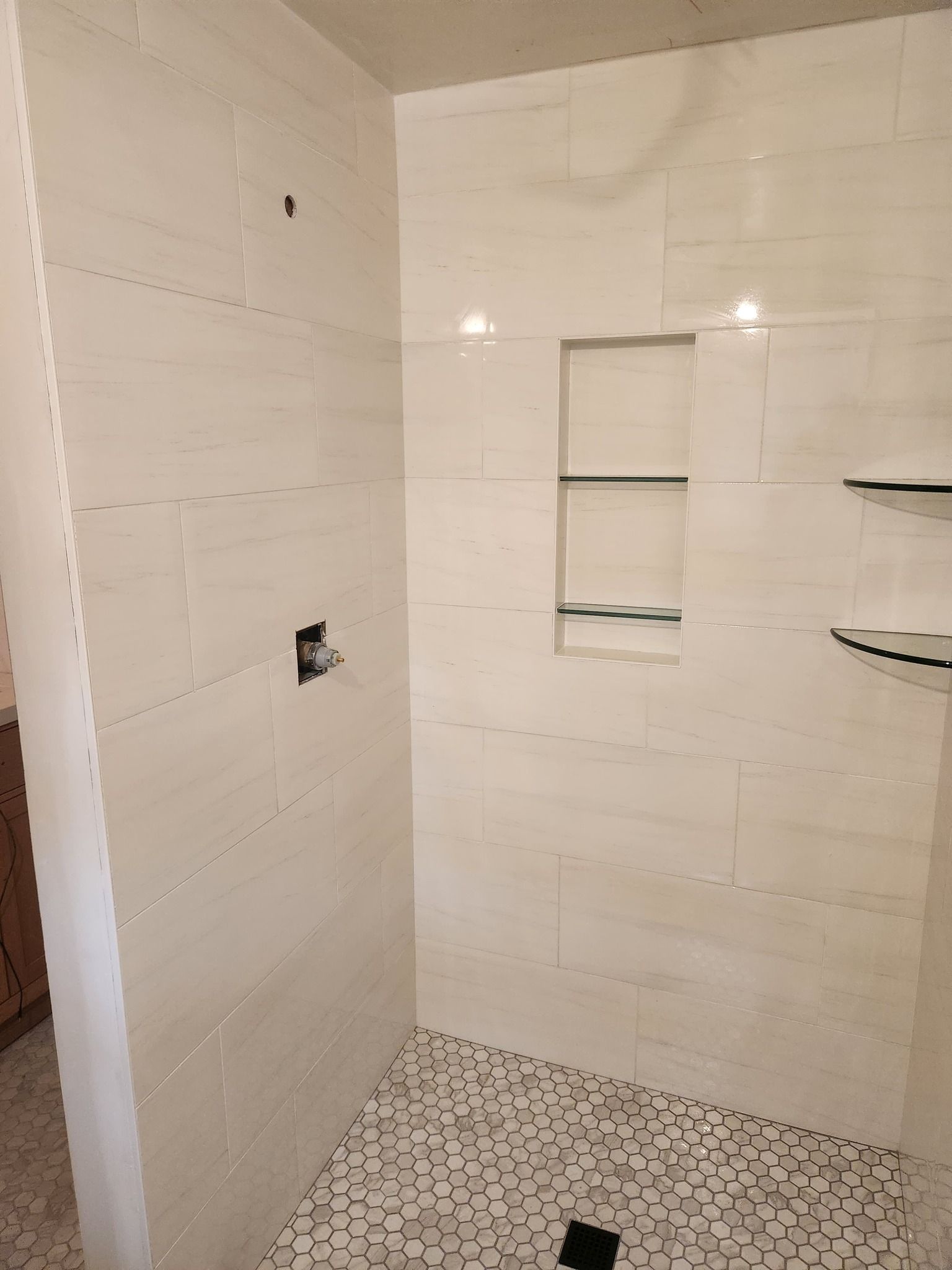 Bathroom shower with white subway tile walls and hexagonal tile floor.