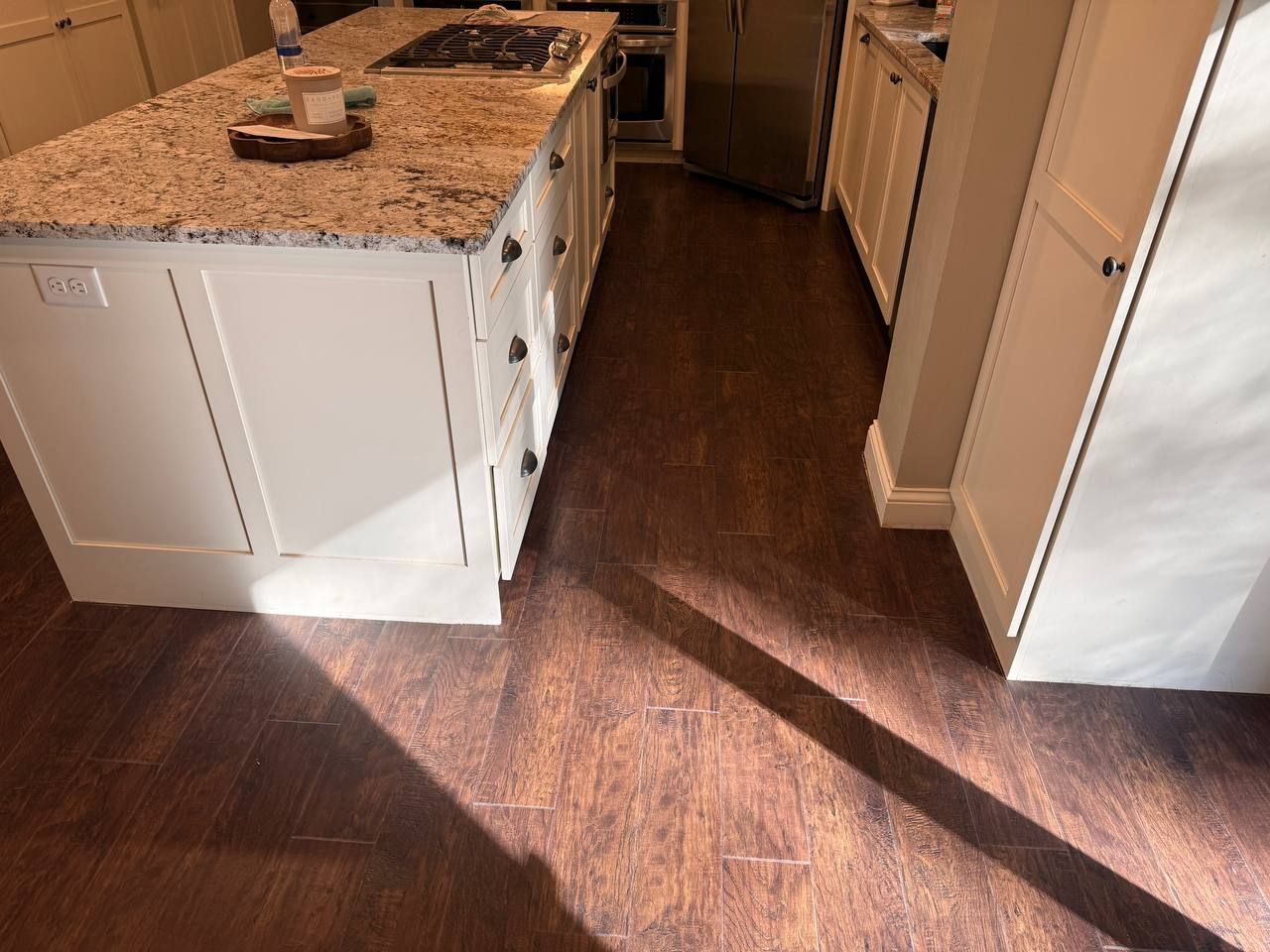 Dark brown luxury vinyl plank flooring installed in a kitchen with white cabinetry and granite countertops.