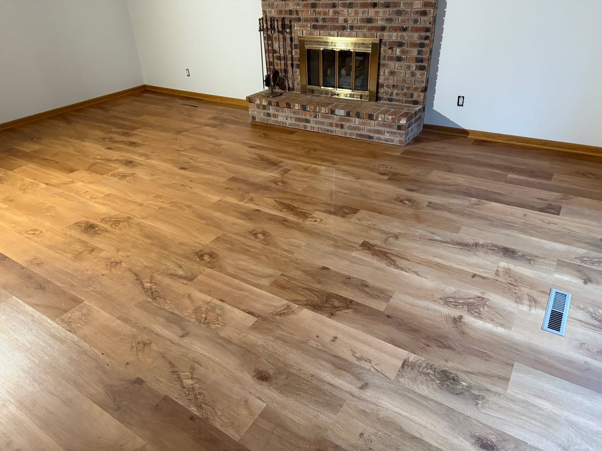 Newly installed LVP plank flooring in a living room with a brick fireplace.
