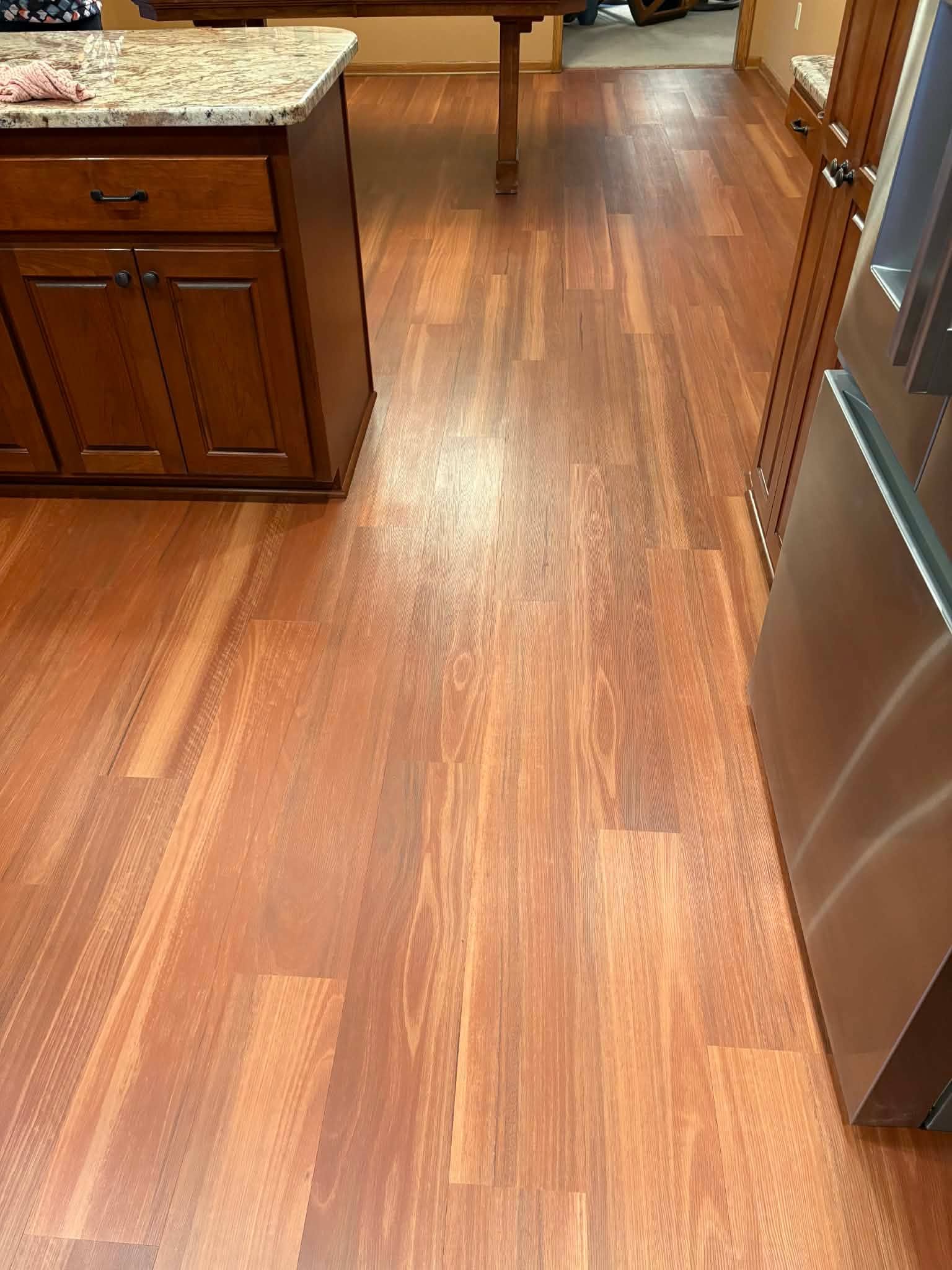 Glued down luxury vinyl plank flooring in warm brown tones installed in a kitchen with wooden cabinetry.