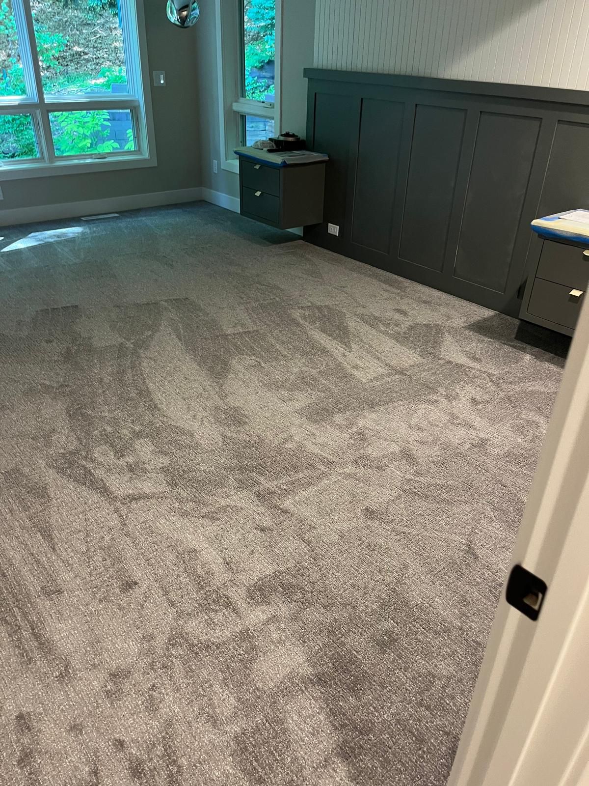 Gray carpet with geometric pattern installed in a bedroom with dark paneling and windows.
