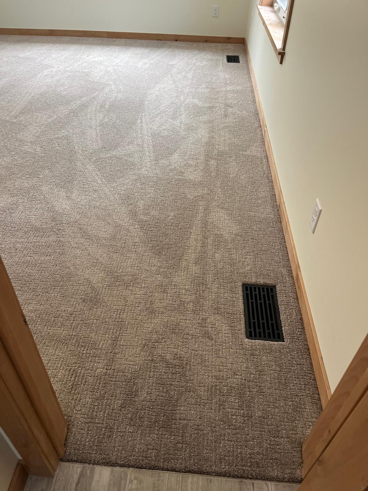 Newly installed light beige carpet in a bedroom with wood trim and floor vents.