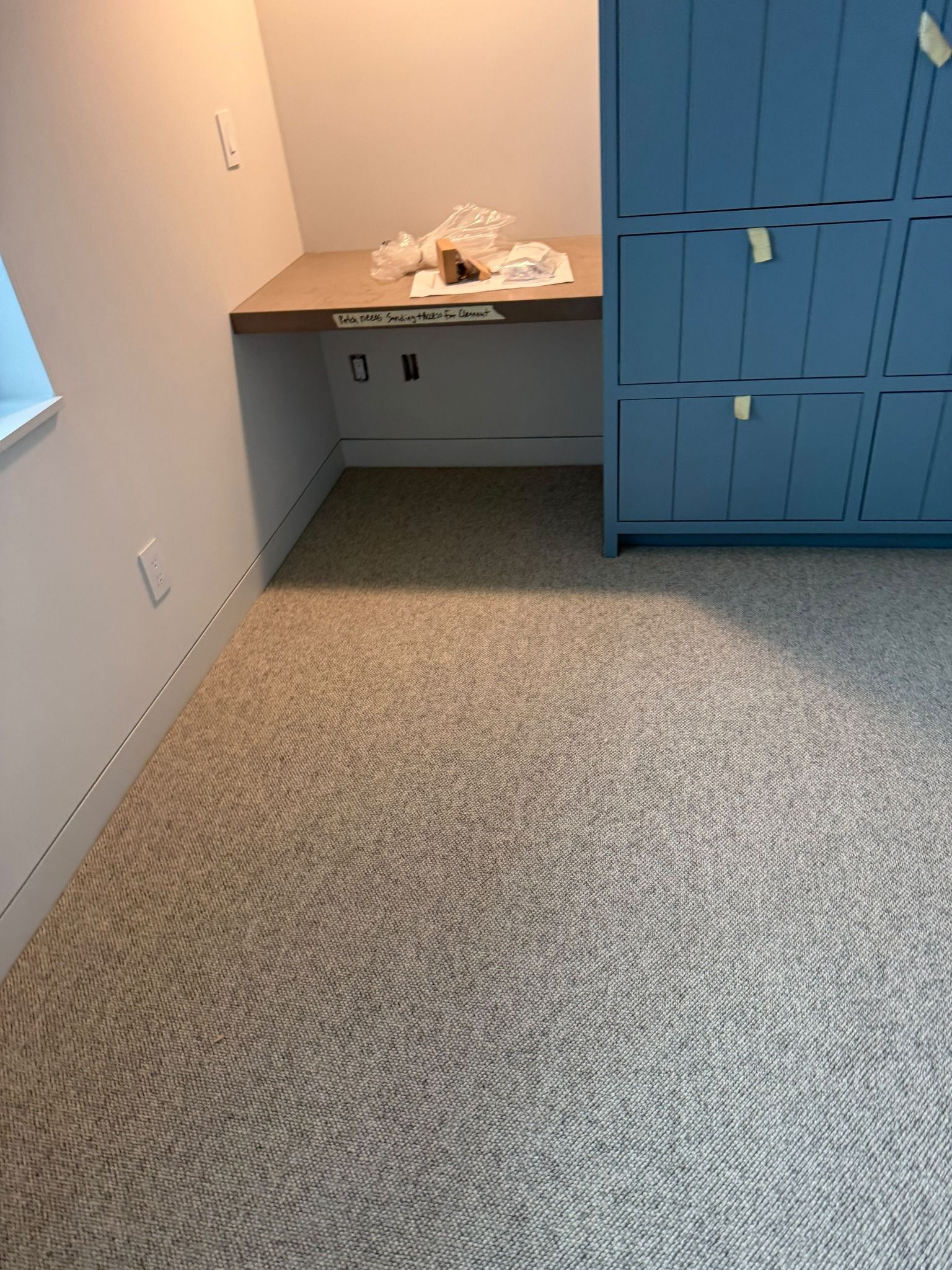 Bedroom with tan and gray carpet installation next to blue closet doors and wooden desk.