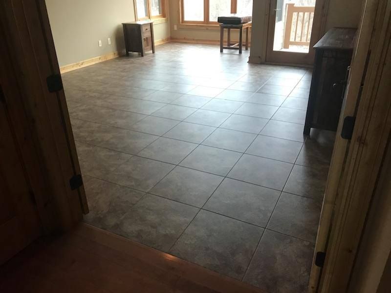 Light gray luxury vinyl plank with grout lines installed in a kitchen with wood trim doorway.