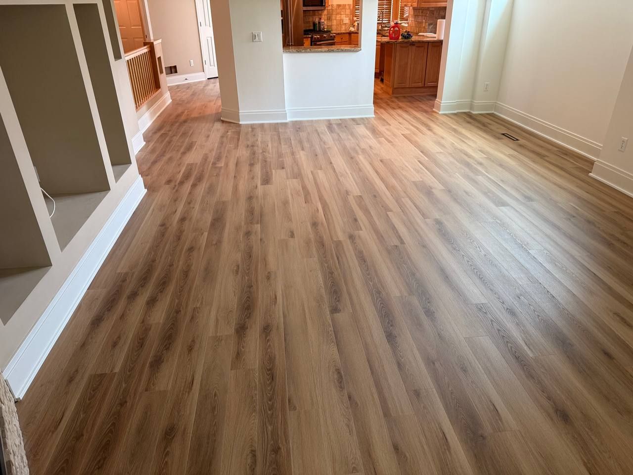 Living room with medium-toned wood-look LVP planks installed in an open floor plan with white trim.