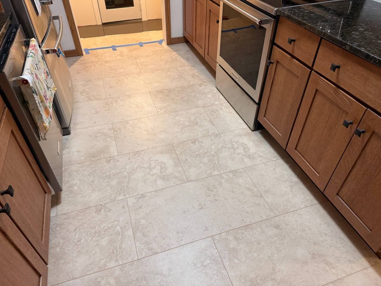 Kitchen flooring with light beige and gray luxury vinyl plank tiles in subway pattern with grout lines.
