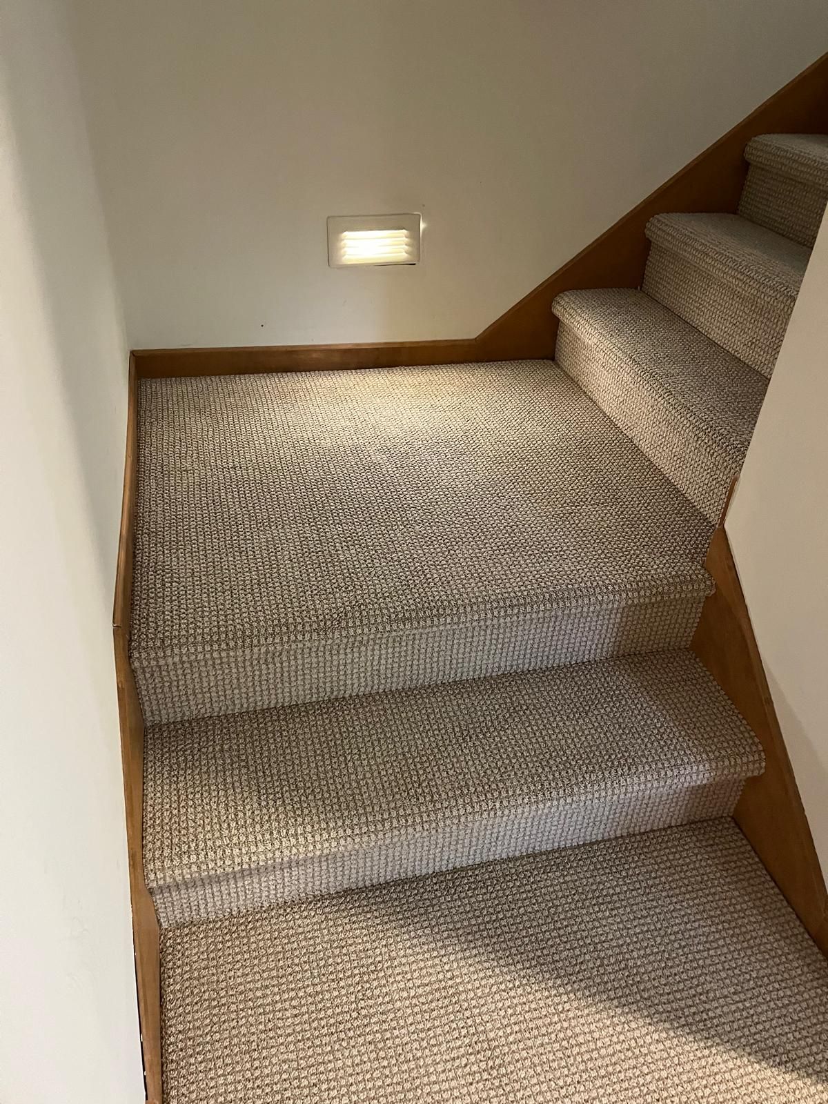 Staircase with beige textured carpet and wood railings leading to an upstairs landing.