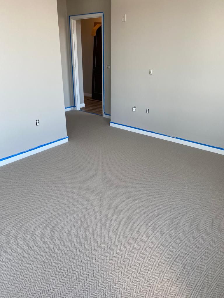 New gray herringbone carpet installation in bedroom with blue tape along baseboard edges.