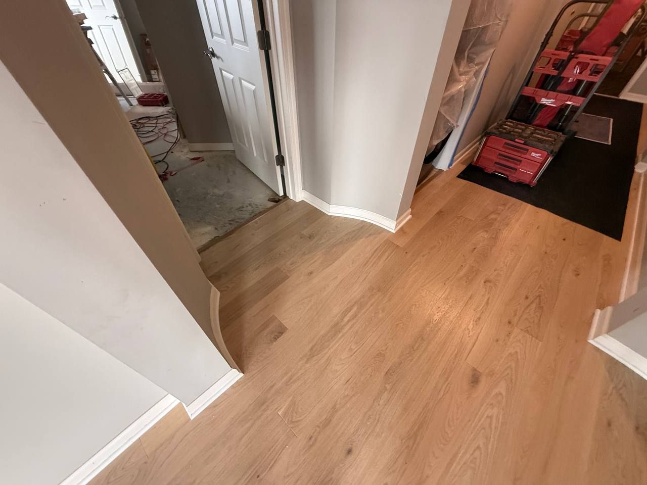 Hallway with light tan hardwood plank flooring and white baseboards leading to doorways.