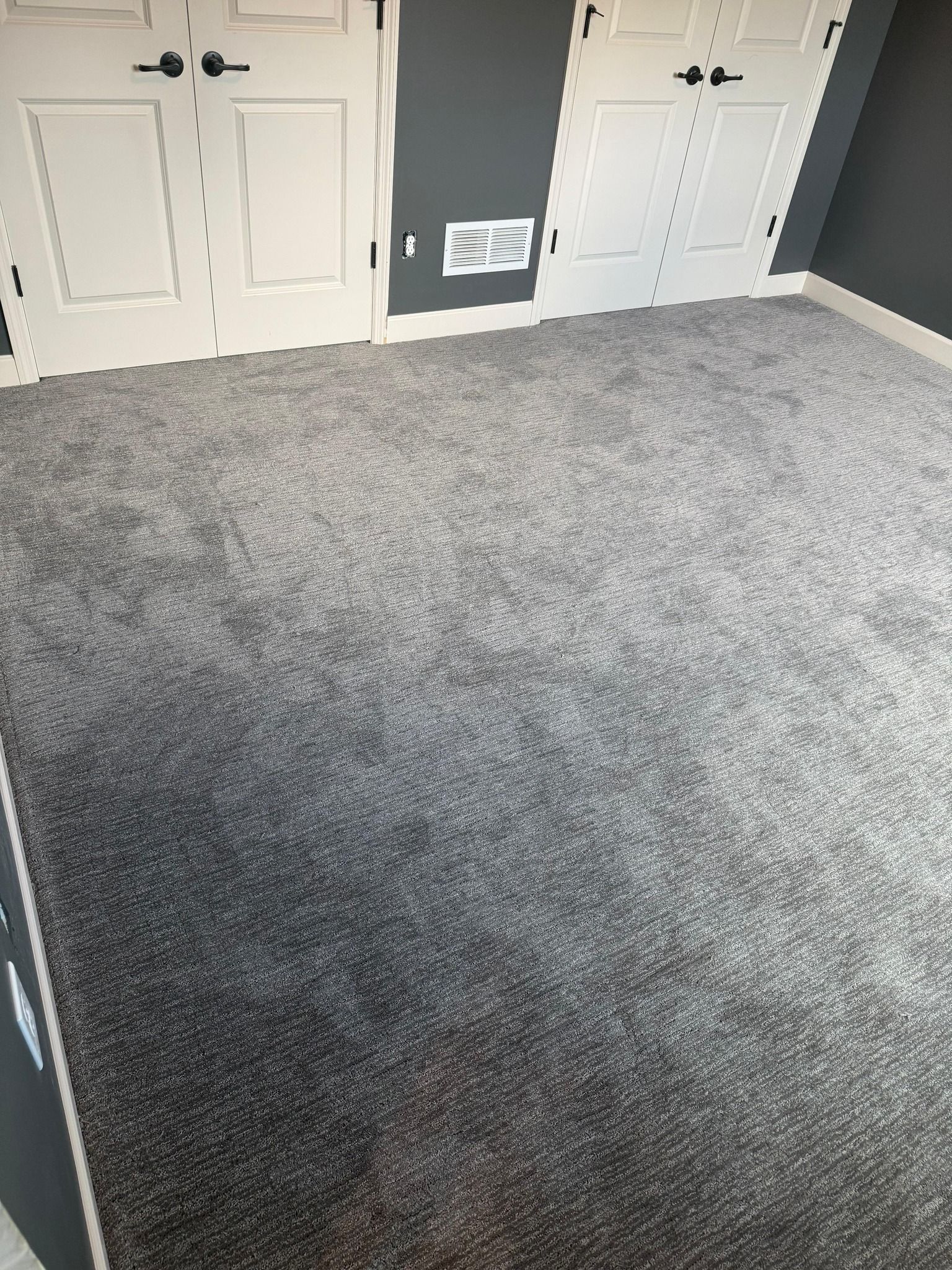 Gray textured carpet installed in a bedroom with white closet doors and dark accent wall.