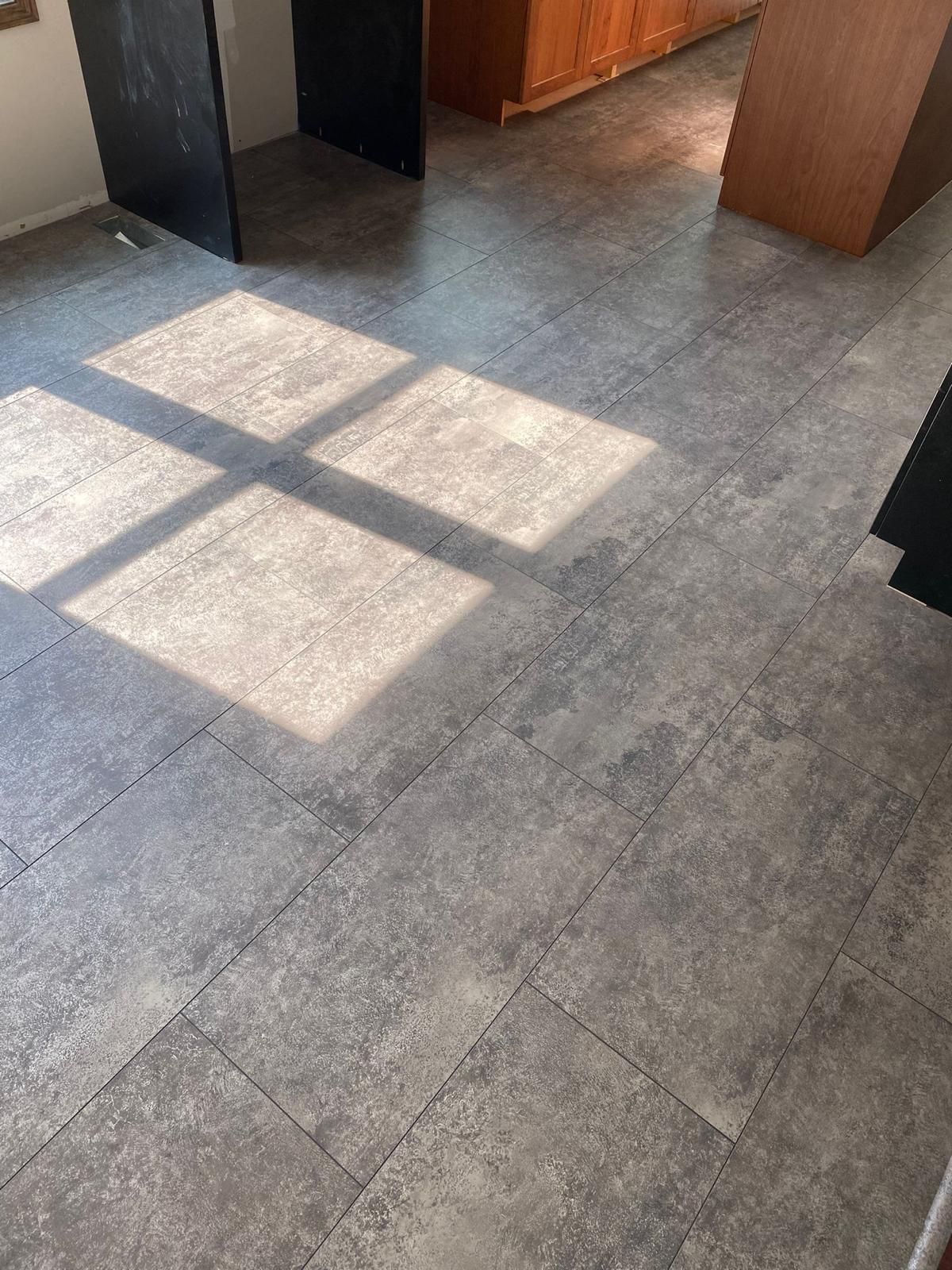 Gray plank LVP with concrete appearance installed in kitchen with wood cabinetry.