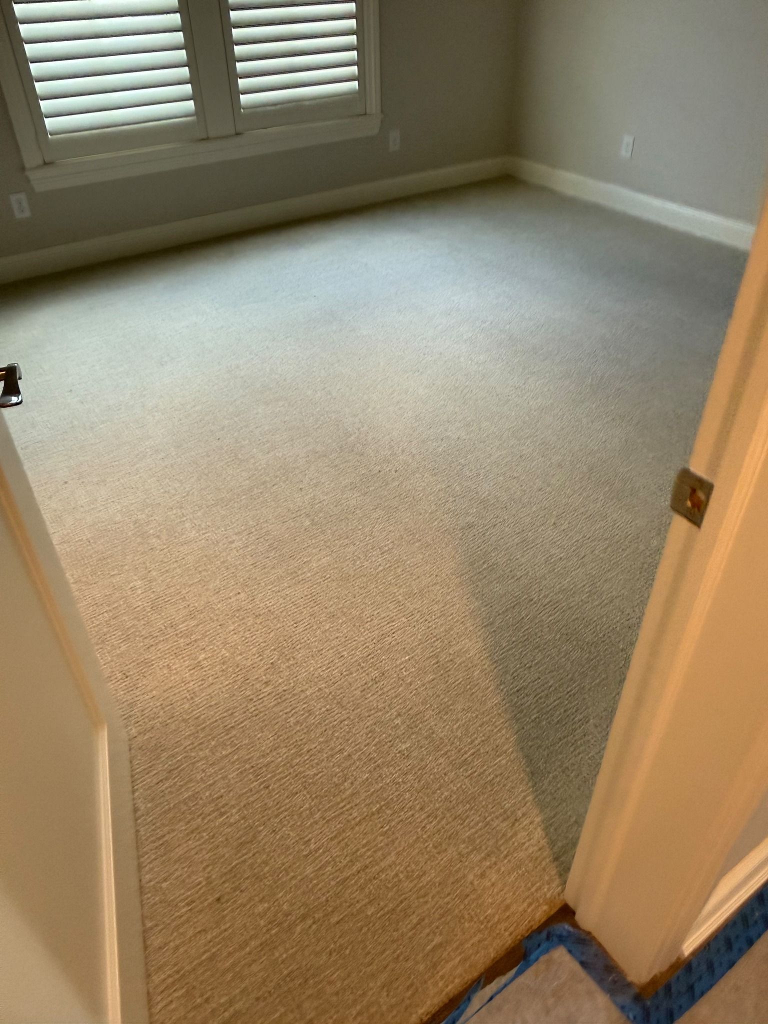 Light beige carpet installed in a bedroom with white trim and shuttered windows.
