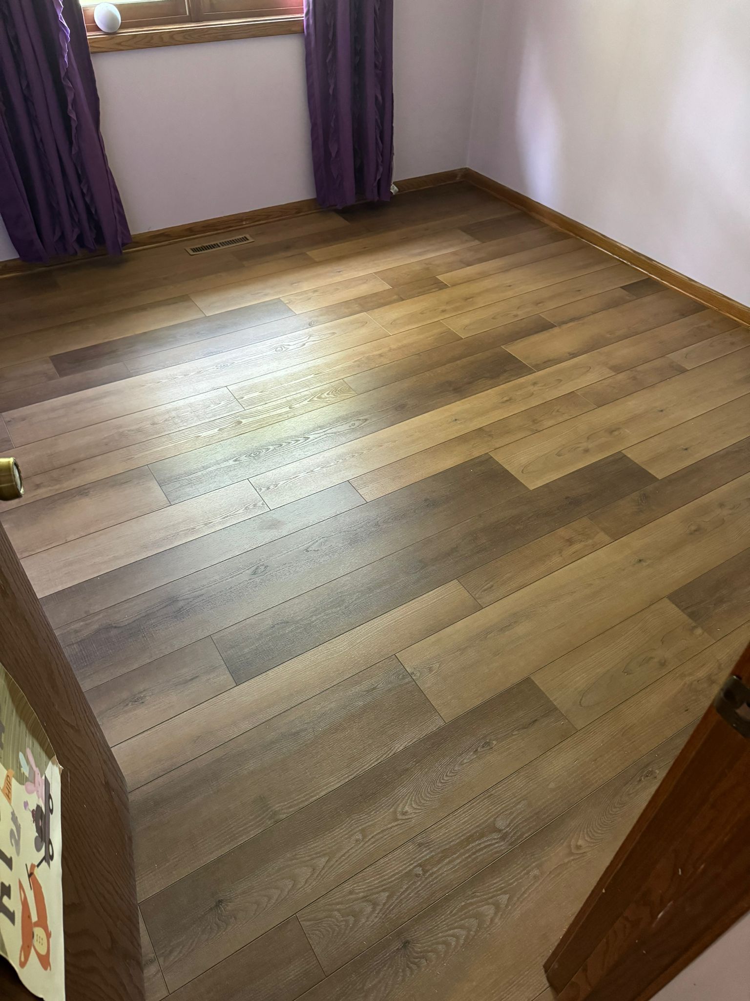 Bedroom with mixed-width LVP planks in varying brown and tan tones installed in staggered plank pattern.