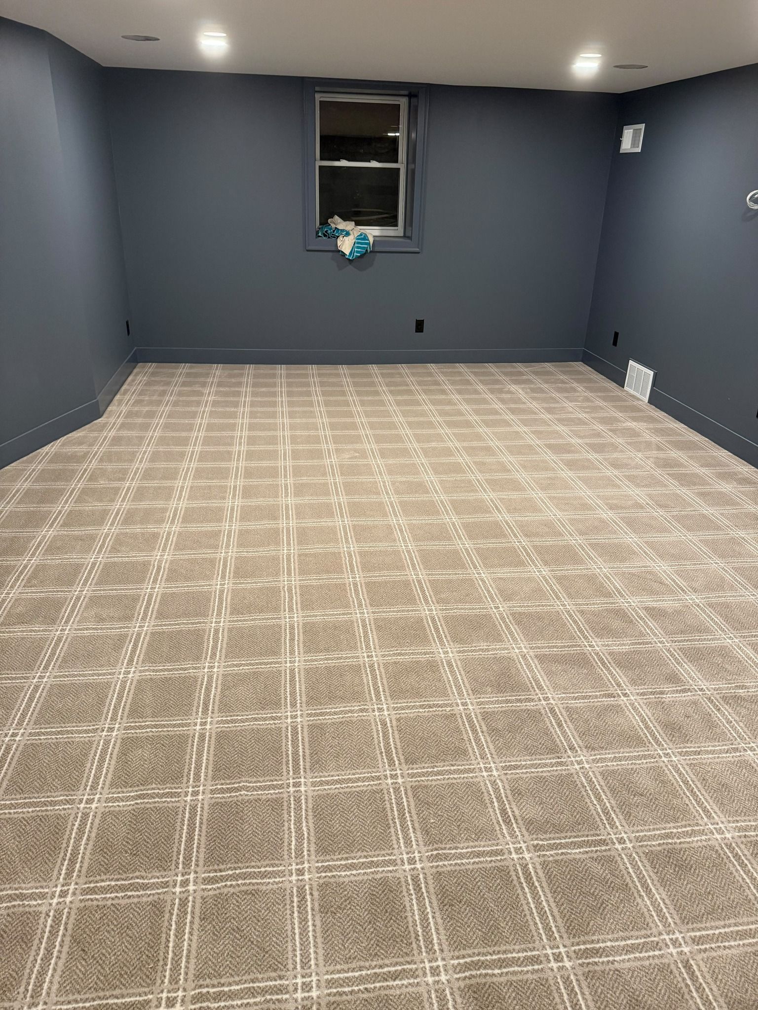Newly installed light beige carpet with cream grid pattern in a basement room with blue walls.