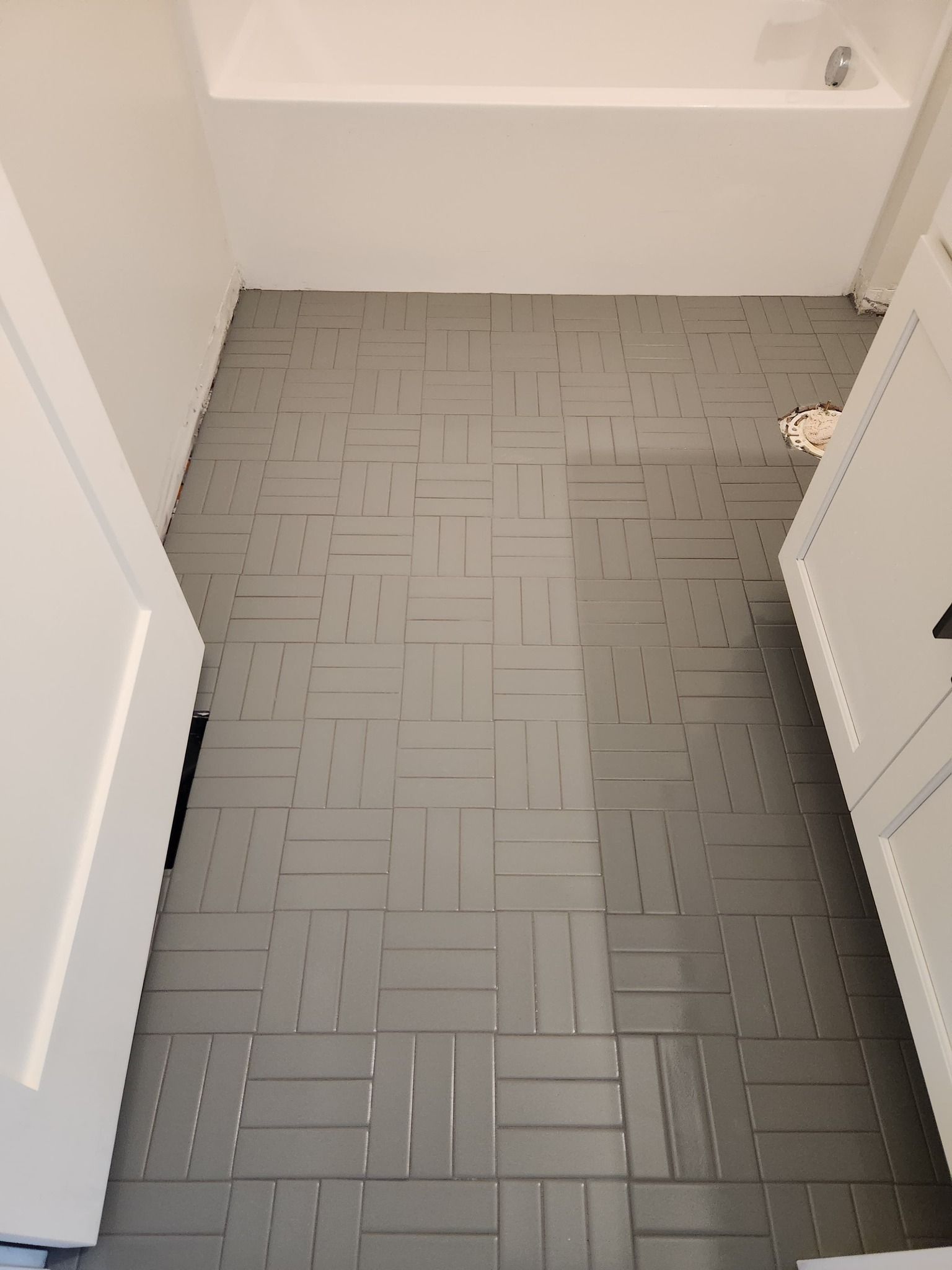 Bathroom floor with gray tile in herringbone pattern beneath white bathtub and walls.