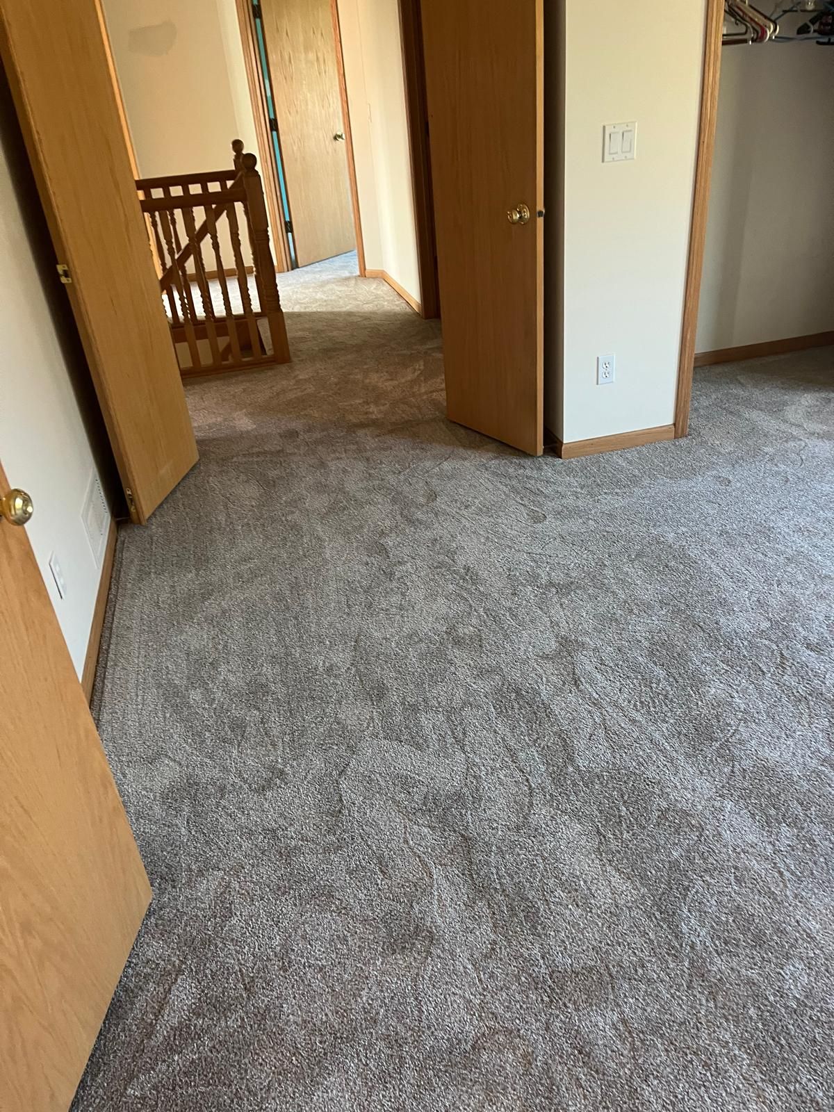 Gray carpet installed in a hallway with wood-framed doorways and white walls.