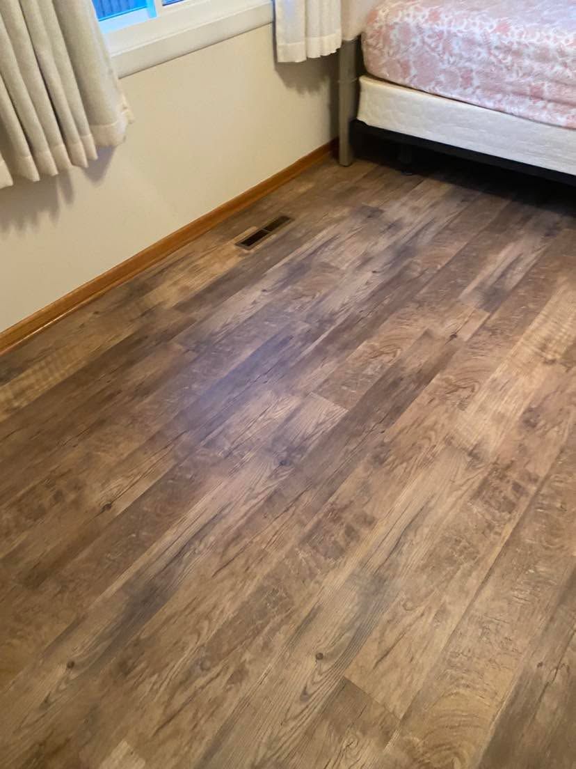 Luxury vinyl plank flooring in a bedroom with wood grain appearance and tan-brown tones.