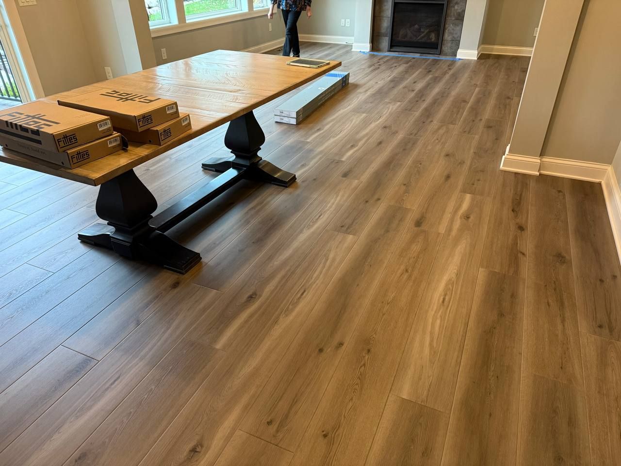 Luxury vinyl plank flooring in medium brown installed in a living room with exposed fireplace and large windows.