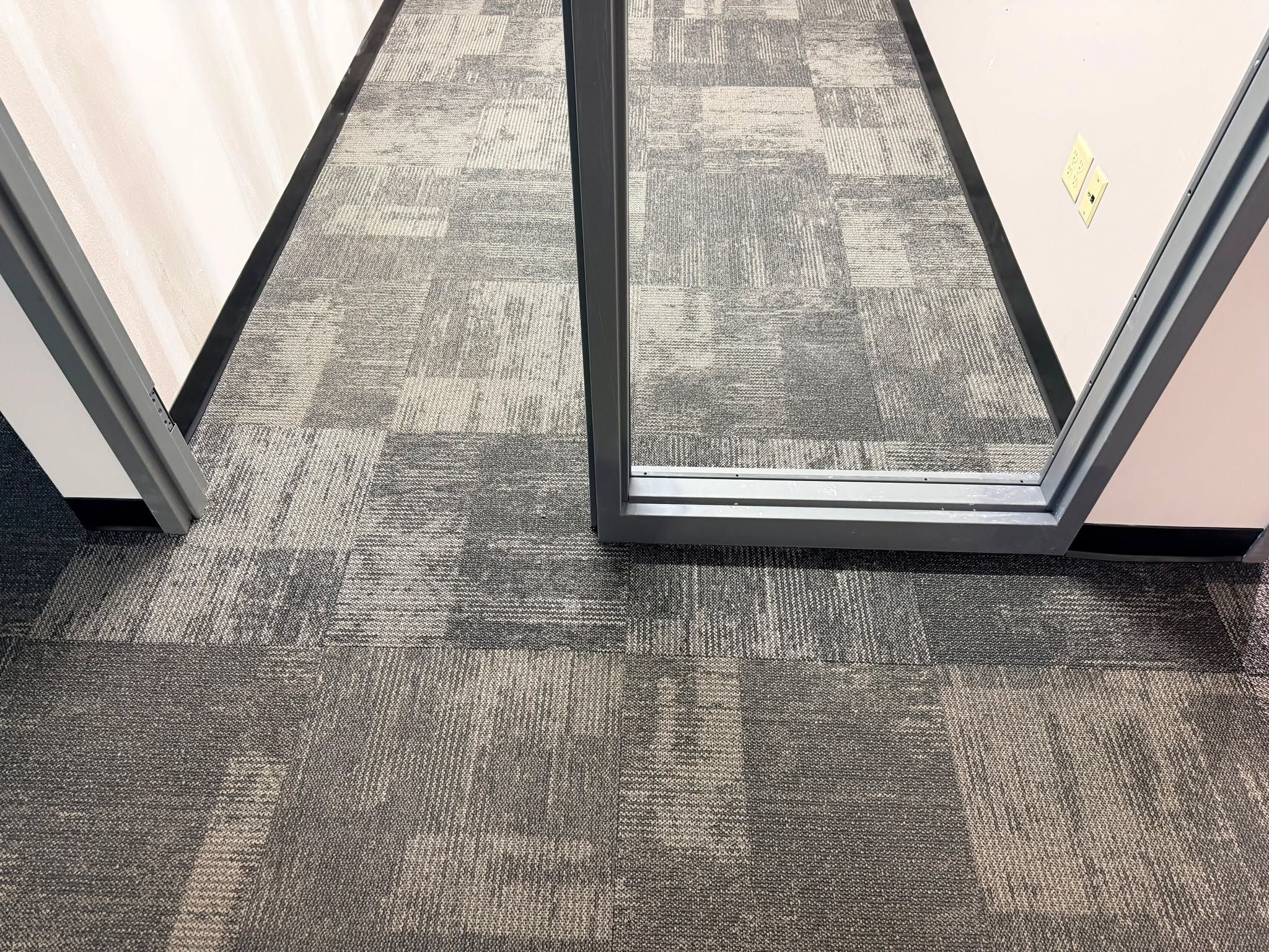 Gray and tan carpet tiles in mosaic pattern installed at office entrance with metal door frame.