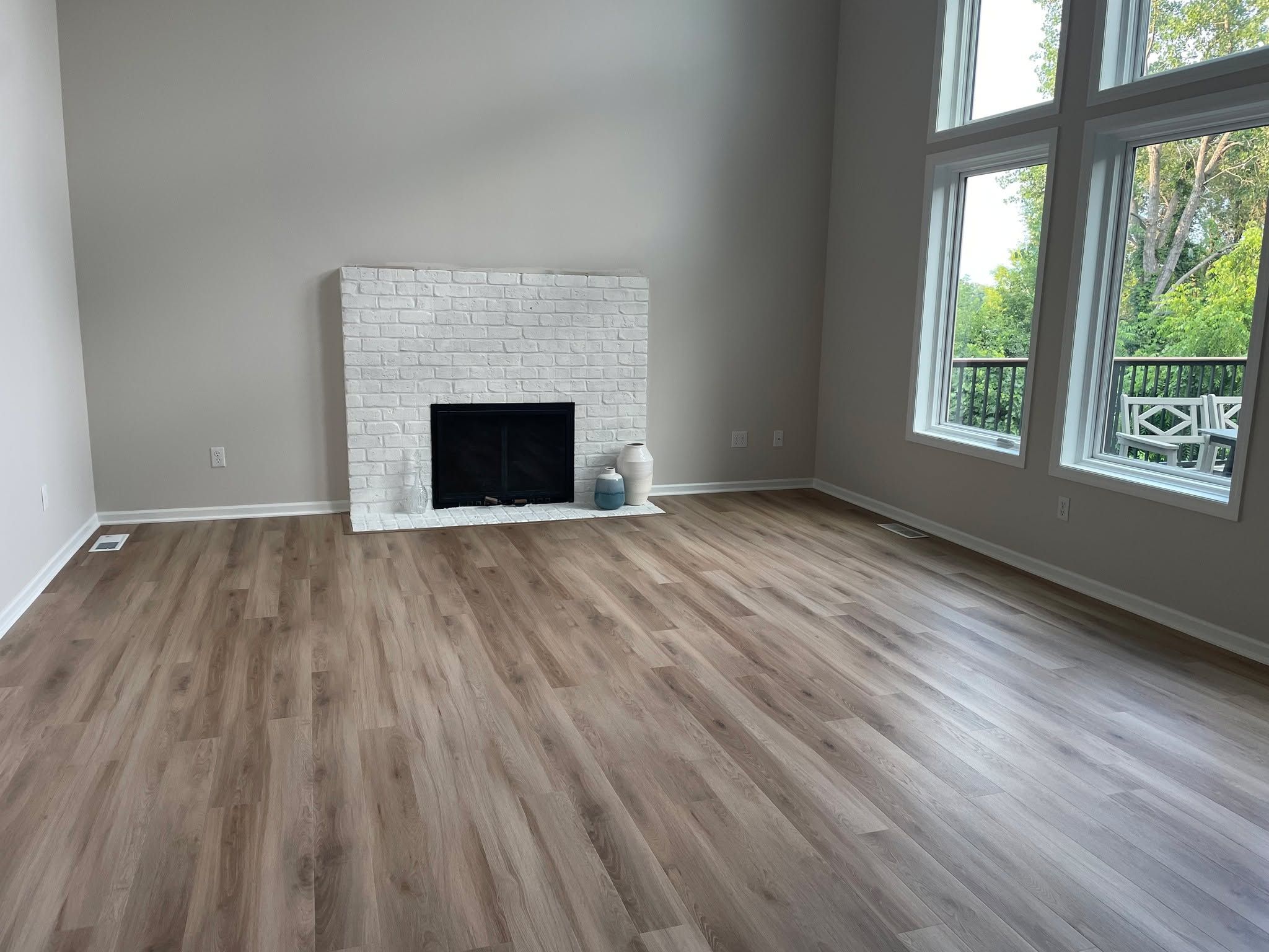 Living room with gray and brown plank LVP flooring and white brick fireplace.