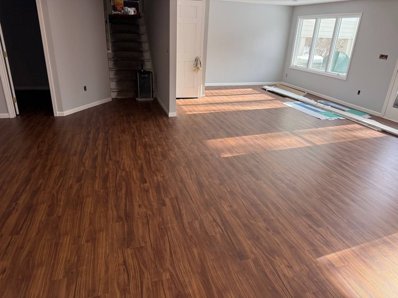 Lower level basement with newly installed medium-brown wood-look LVP planks in a room with white walls and large windows.
