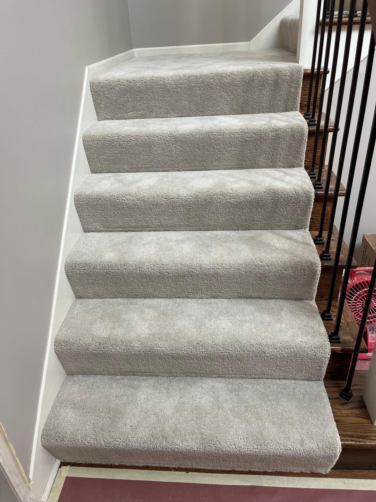 Light beige carpet installed on staircase with white walls and dark wood railing.