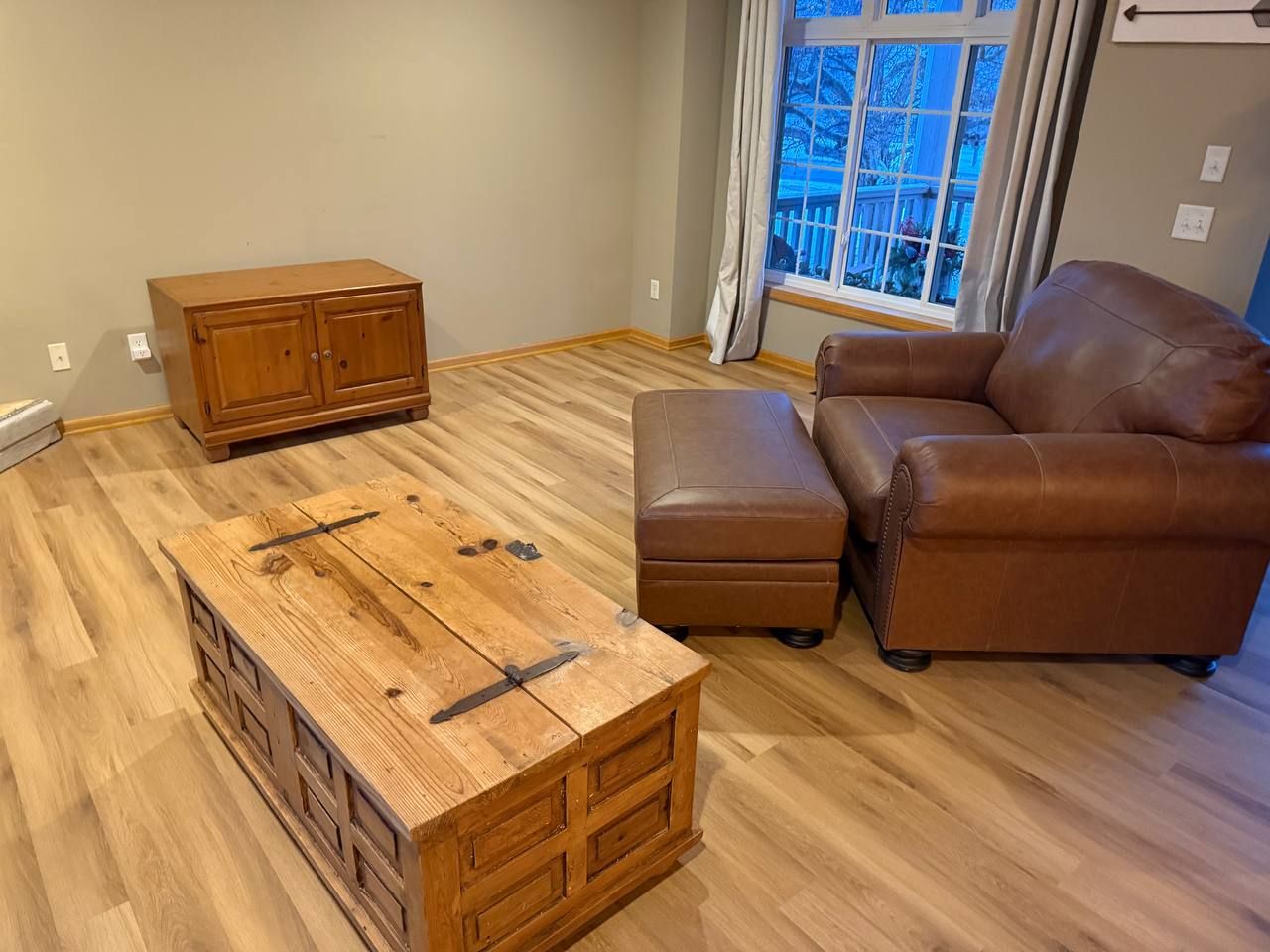 Light tan plank LVP flooring installed in living room with furniture and large windows.