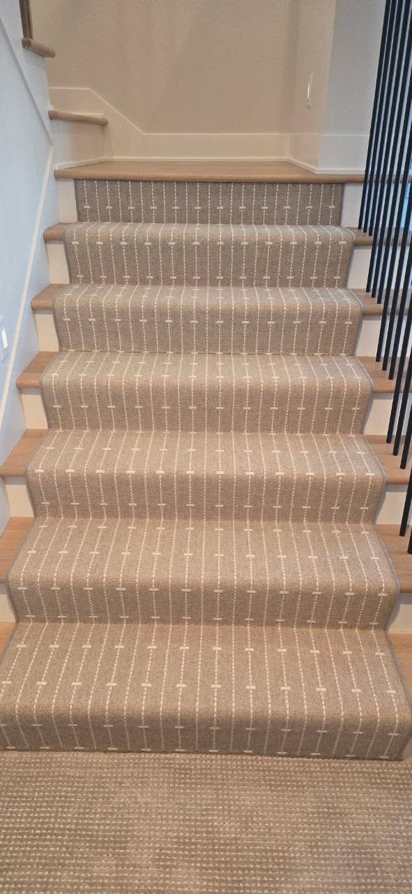 Staircase with tan and white striped carpet runner and wood stair nosing.