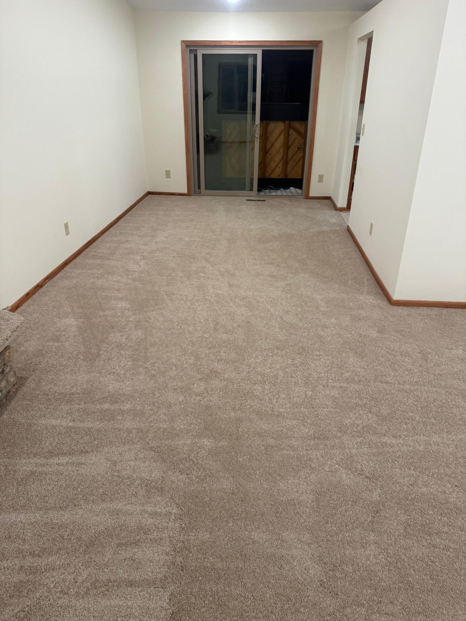 New beige carpet installed in a bedroom with wood trim and sliding glass door.