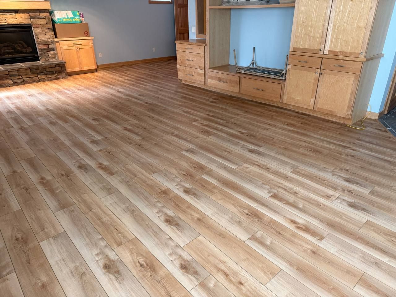 Living room with light tan and brown plank LVP flooring installed throughout the space with built-in wooden cabinetry and fireplace visible.