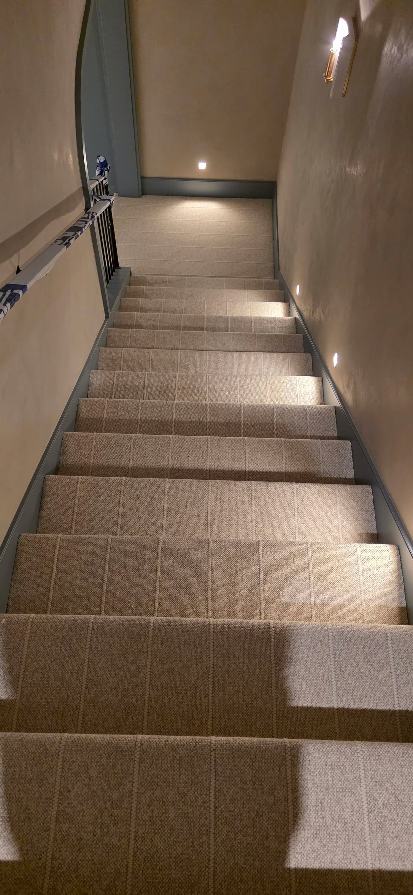 Staircase with tan and brown patterned carpet and recessed lighting along the sides.