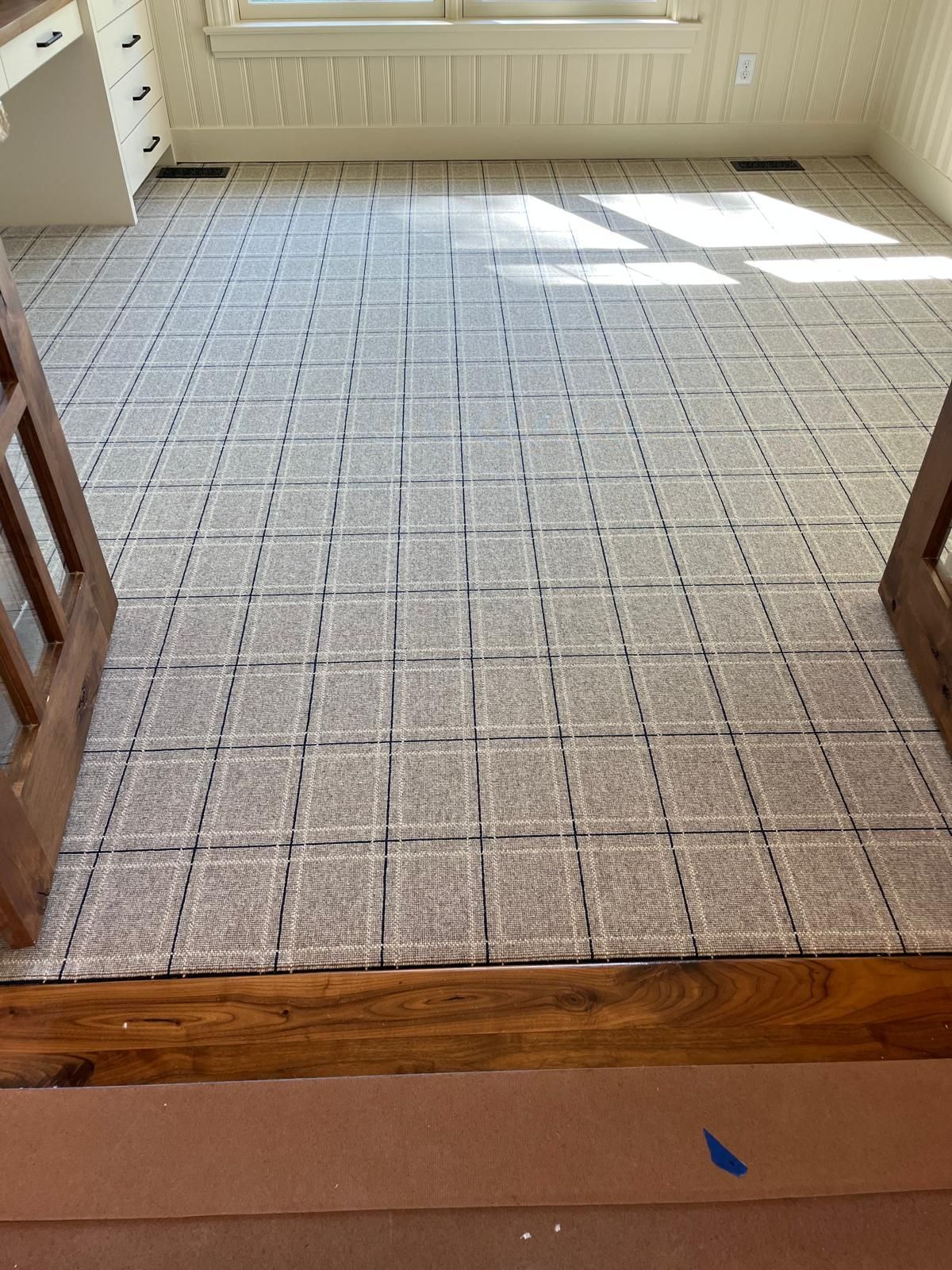 Beige and gray patterned carpet with blue grid lines installed in an entryway with natural light from above.