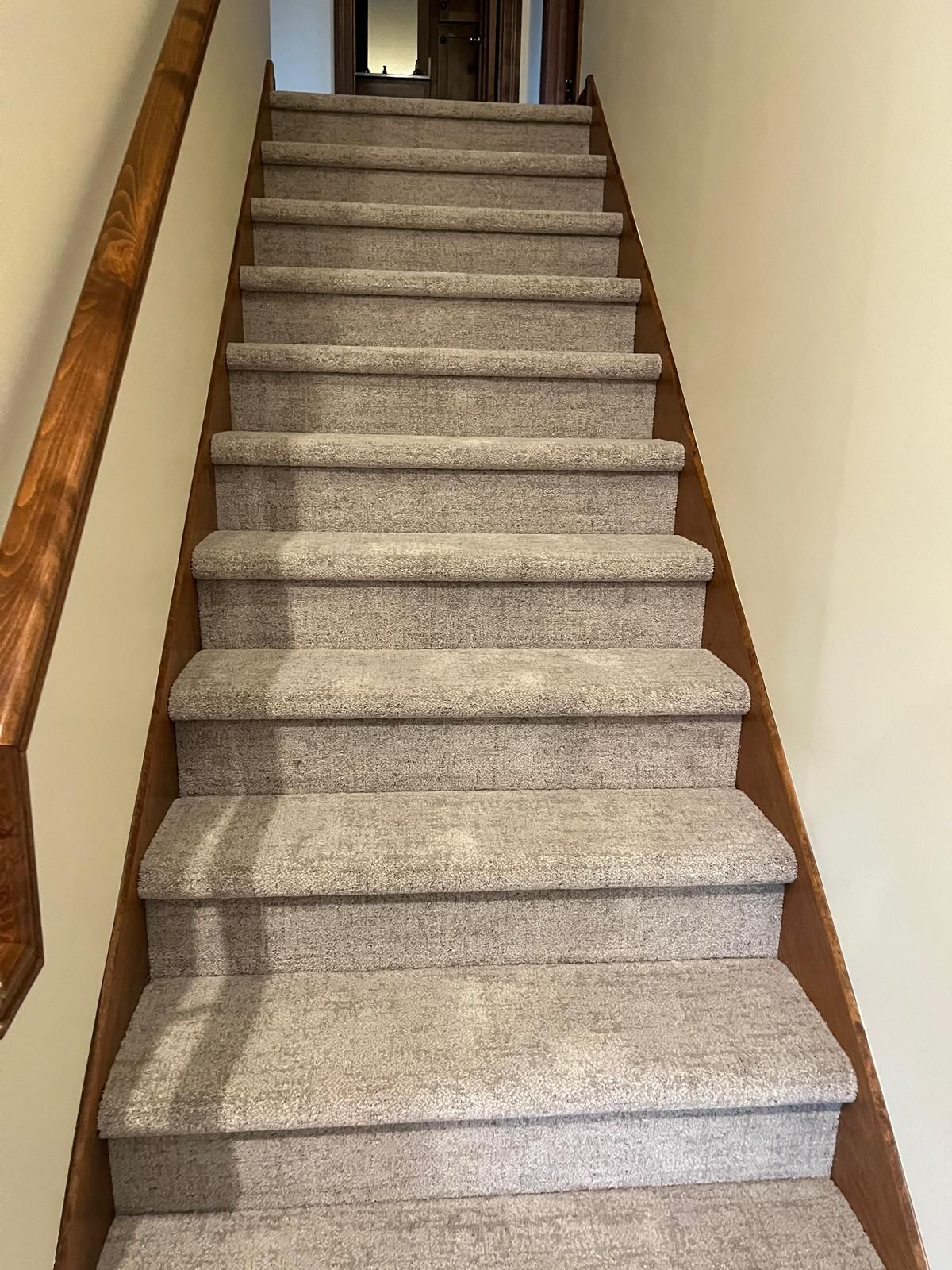 Carpeted staircase with beige carpet runner and wood handrail in residential home.