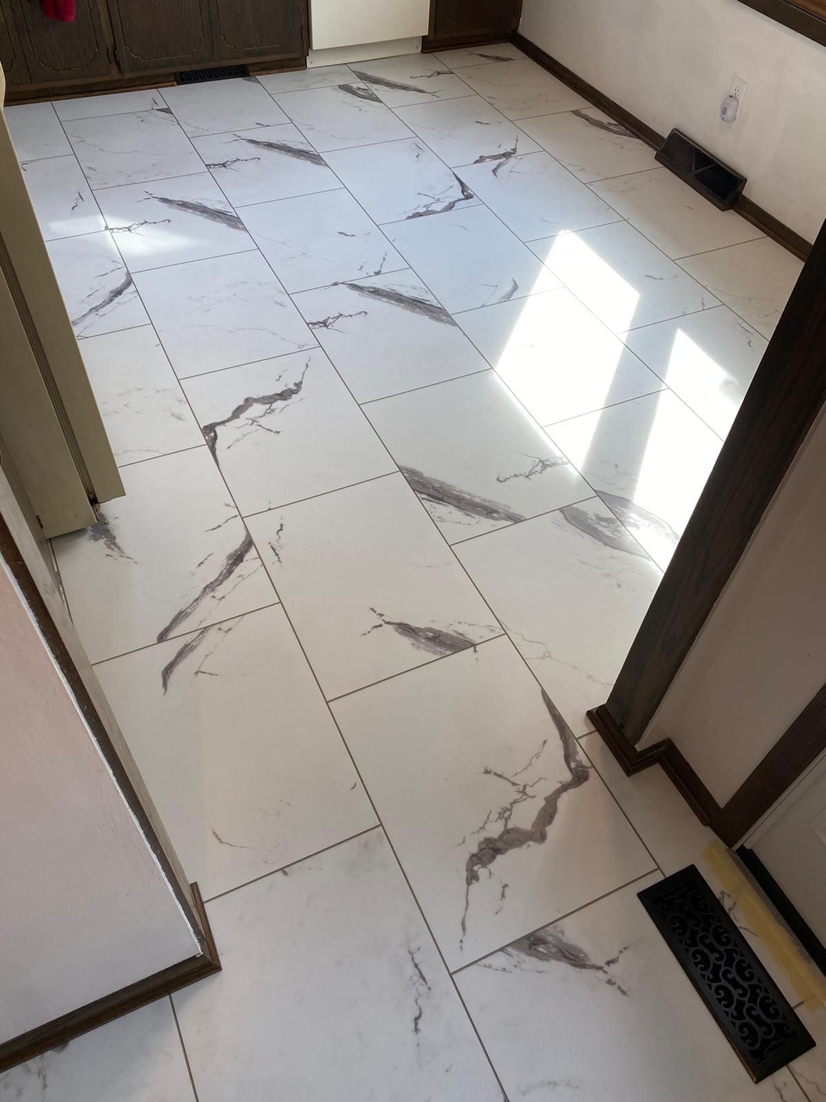 Light white and gray marble-look LVP flooring installed in a kitchen with dark cabinetry.