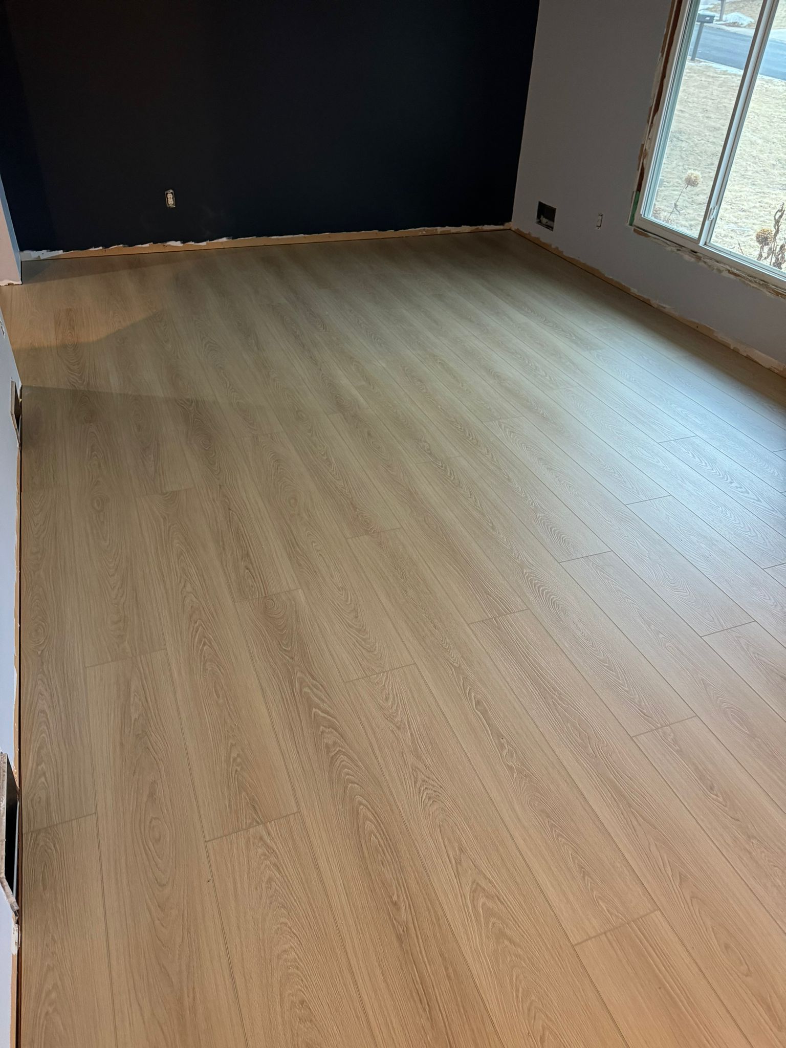 Light tan plank LVP flooring installed in a living room with large windows and blue accent wall.