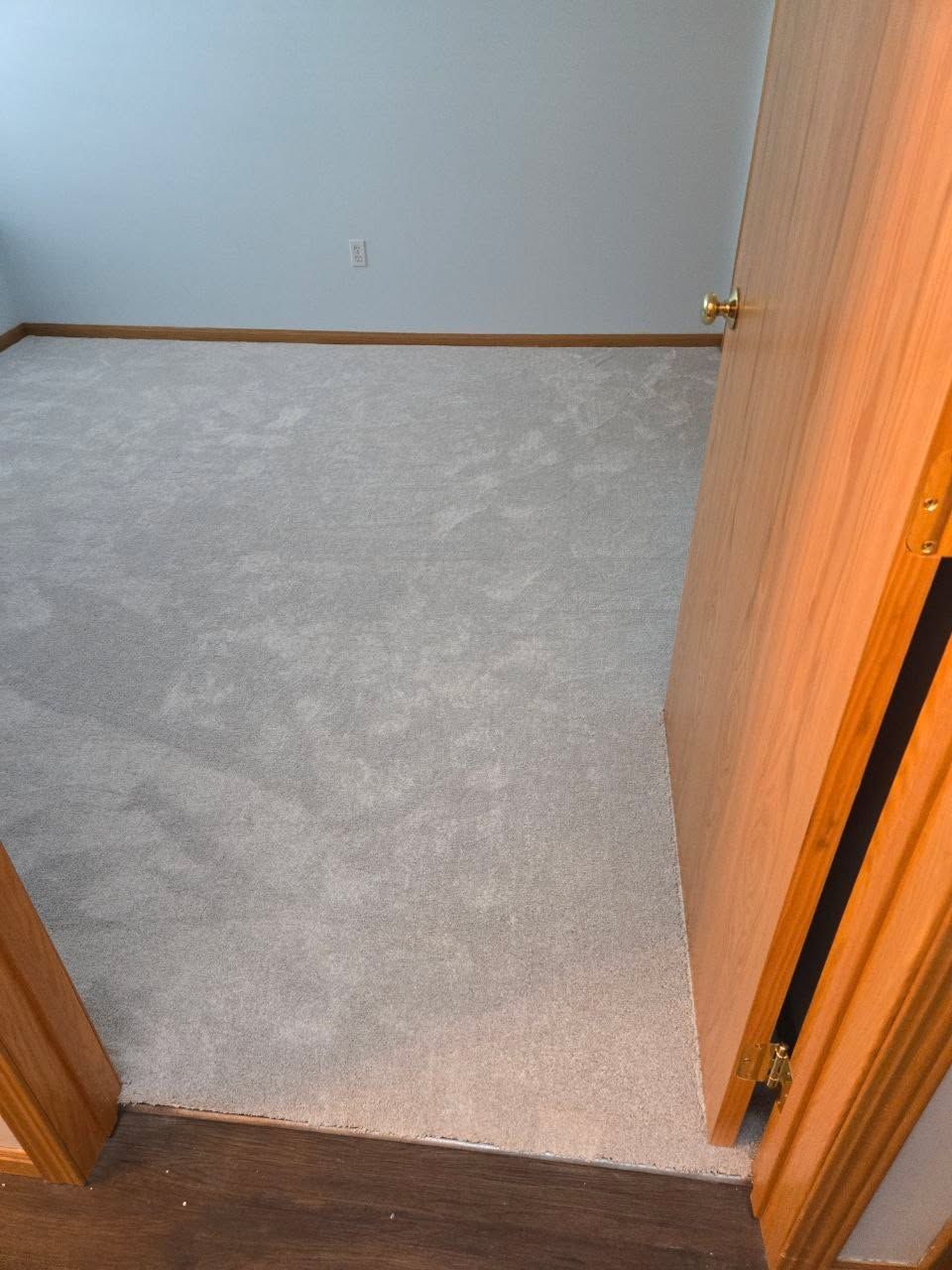 Gray carpet installed in a bedroom with wood door frame and baseboard trim visible.