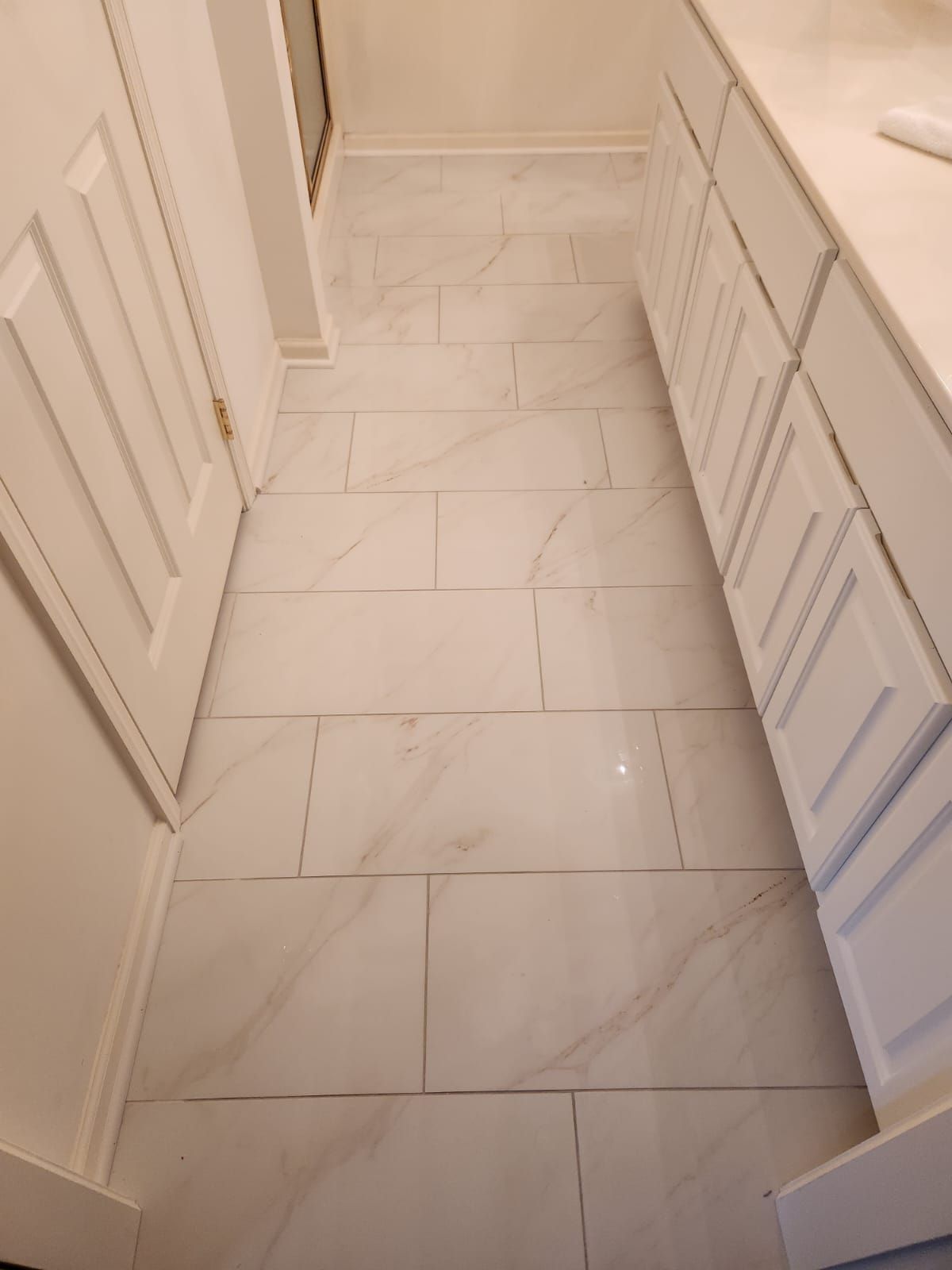 Light marble-look tile flooring installed in a bathroom hallway with white cabinetry on both sides.