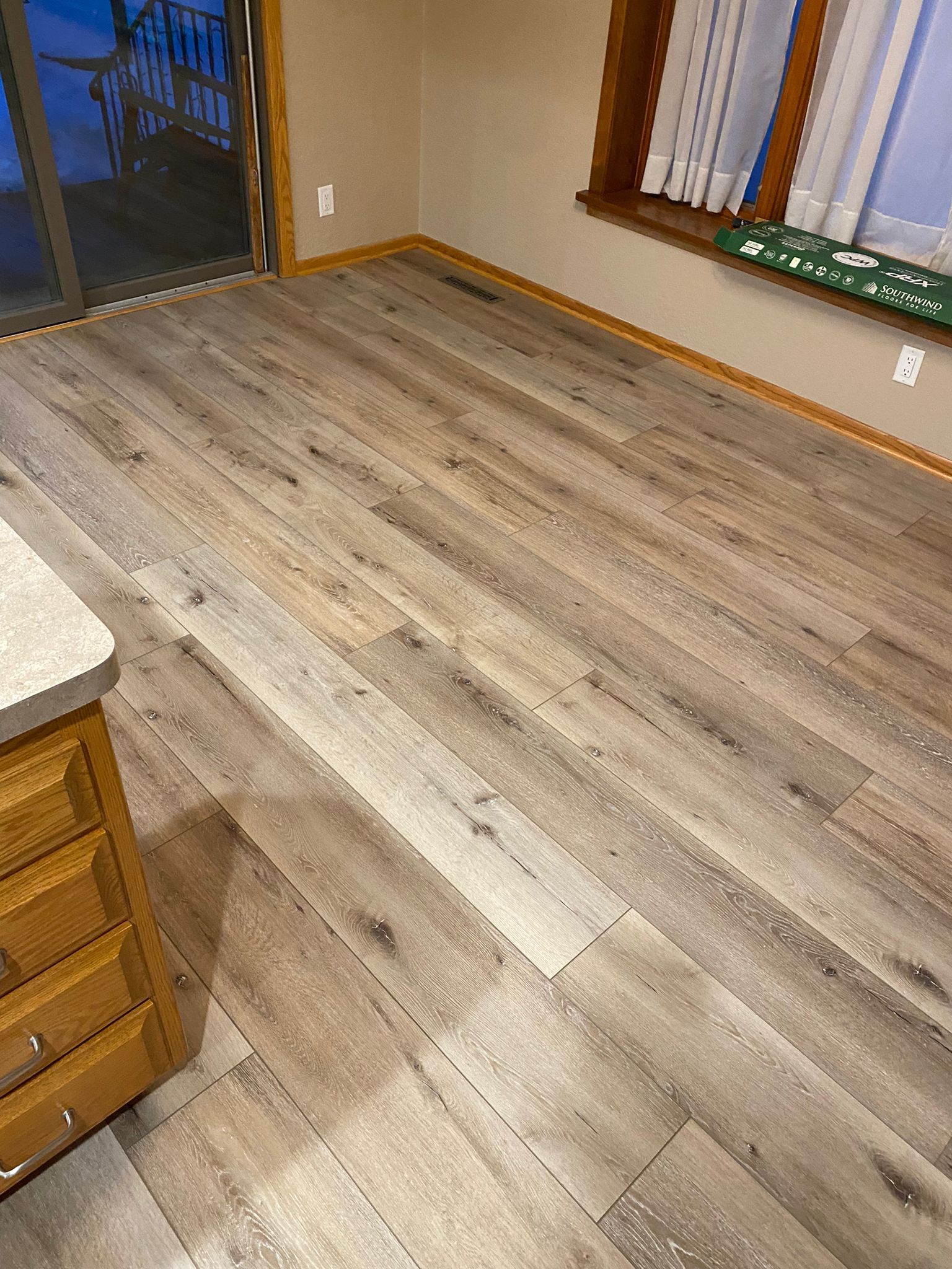 Light gray and brown wood-look LVP planks installed in a living room with wood trim and large windows.