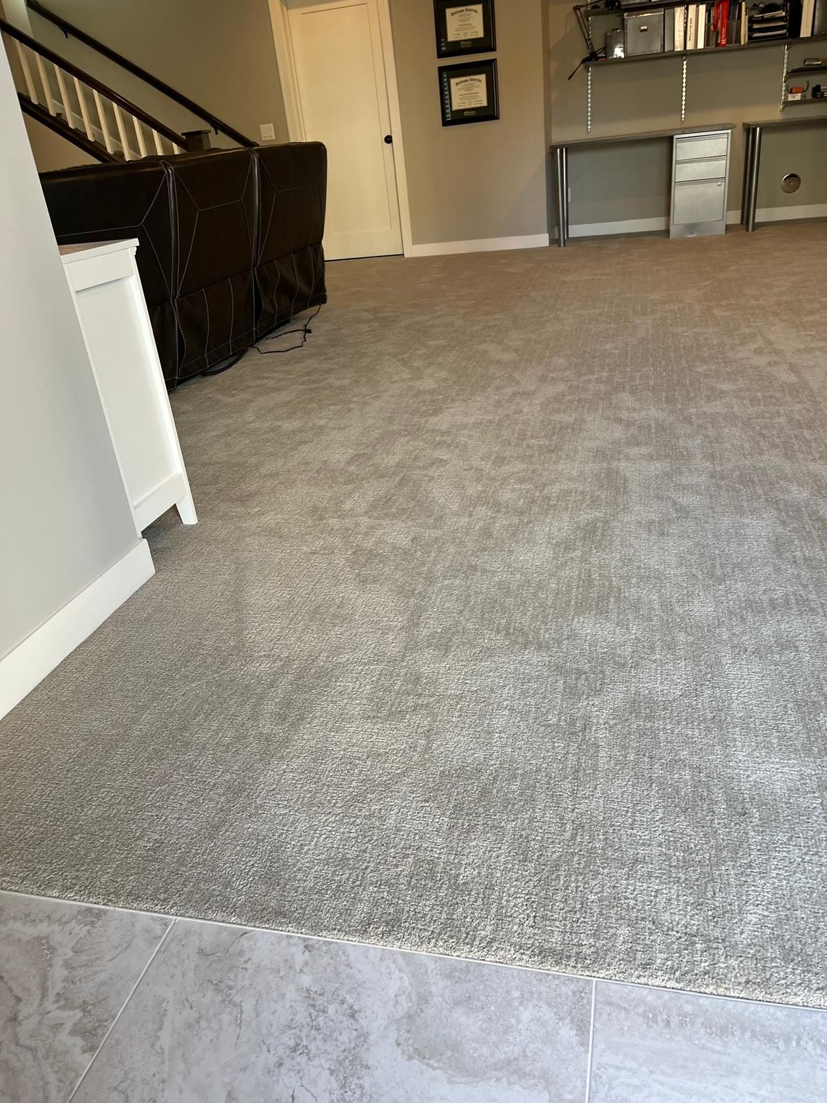 Gray carpet installed in a basement room with white baseboard trim and a transition strip to tile flooring.