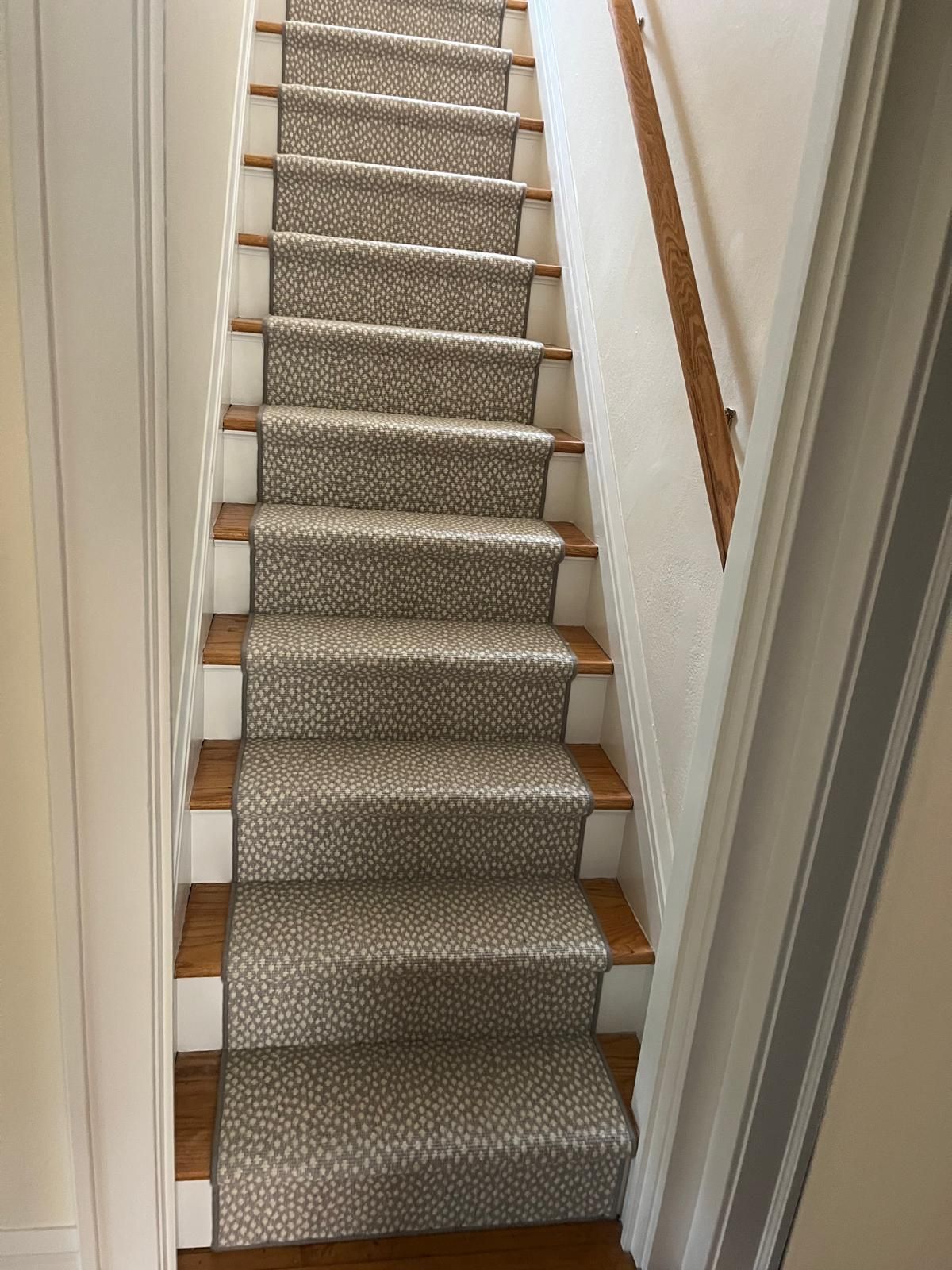 Carpeted staircase with gray patterned wool runner, wood treads, and white painted risers.